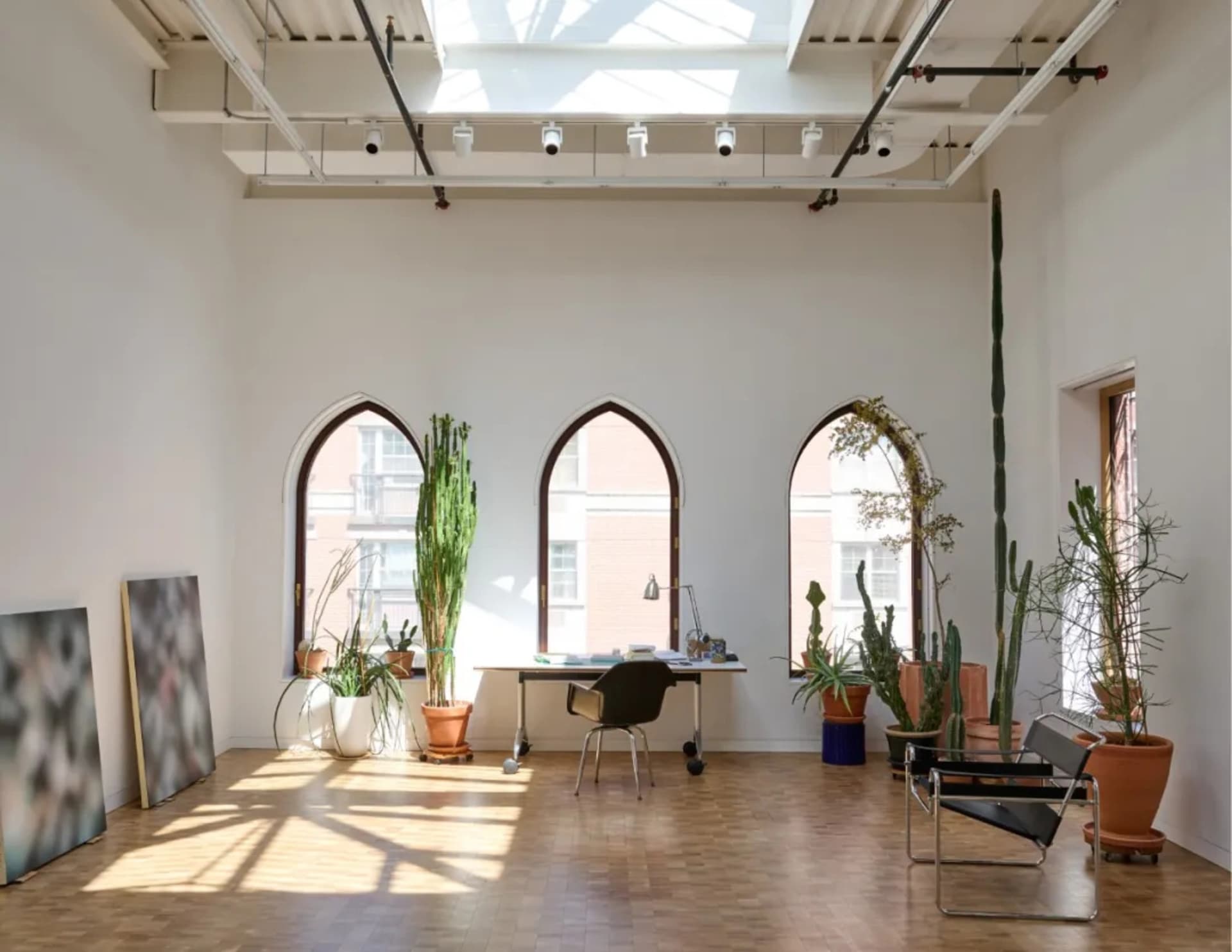 A bright and inviting living area with high ceilings, modern design, and various potted plants, chairs, and a dining table