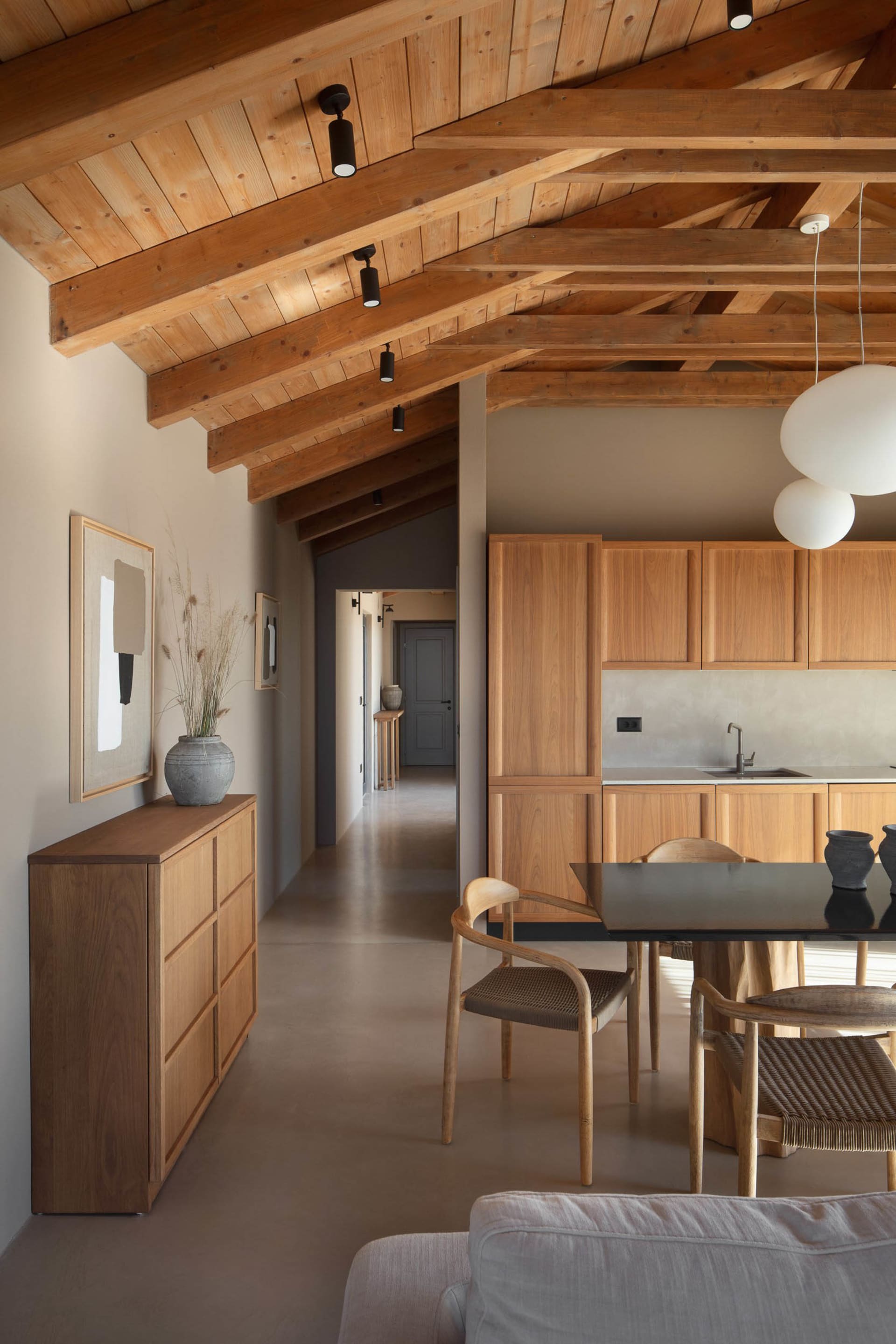 Open modern living area with wooden floors and walls, featuring a dining table and chairs, and decorative vases