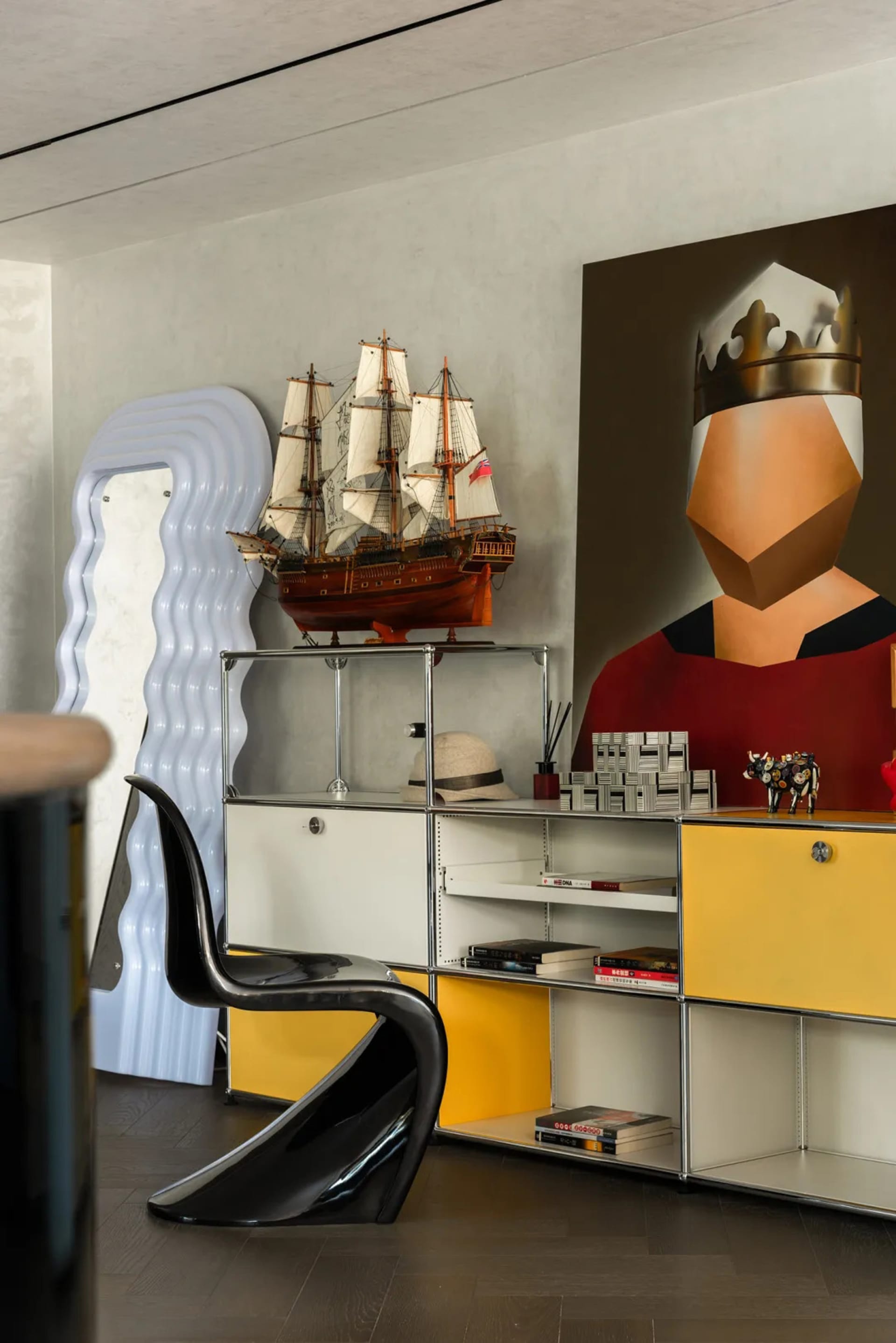 Office space with a desk, chair, paintings, and a boat model, featuring yellow and white walls and a warm atmosphere