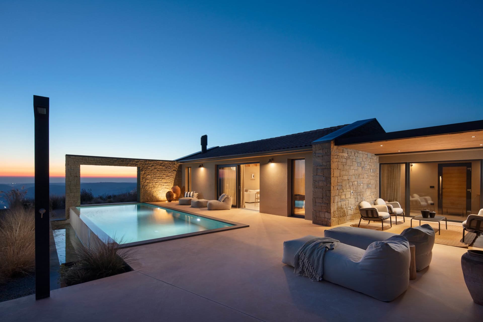 A serene modern house with a stone exterior, a large pool, and outdoor seating areas