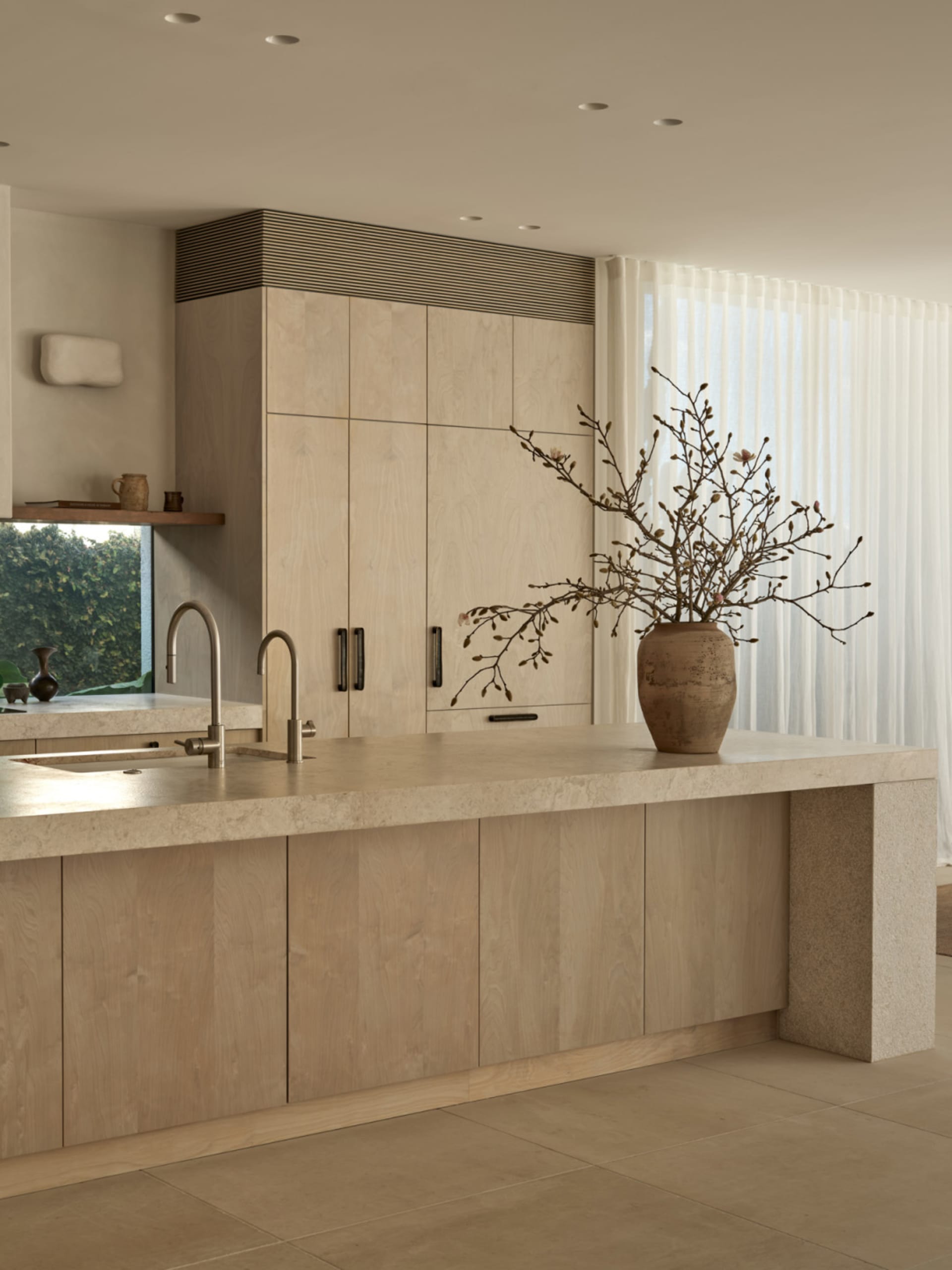 A clean and well-organized kitchen with white cabinets and countertops, a vase with flowers, and two potted plants, creating a bright and inviting atmosphere