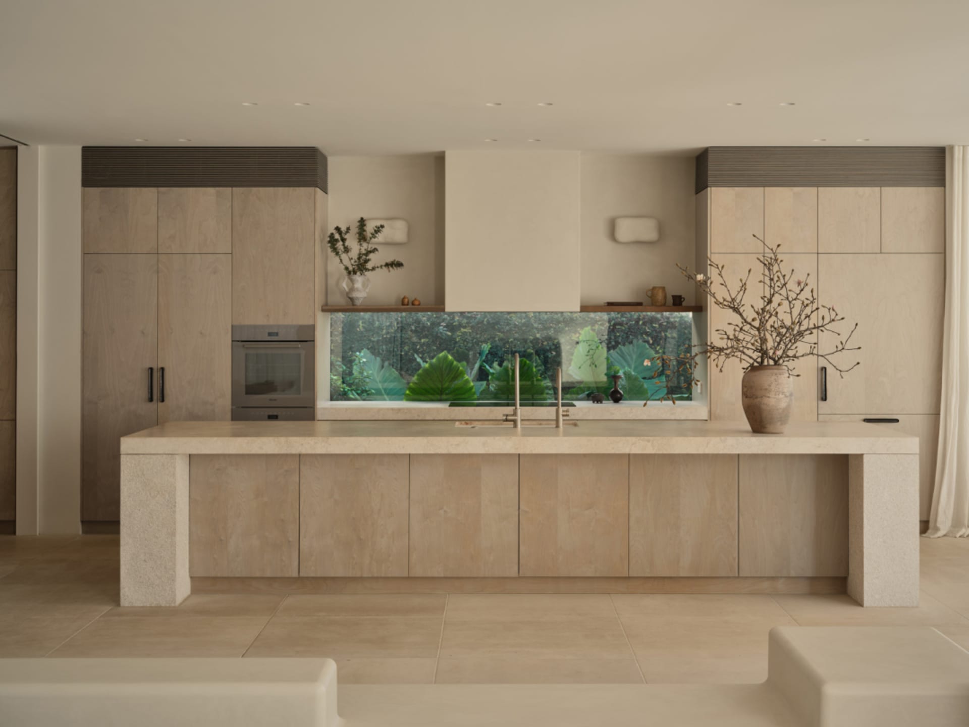 Open kitchen with a large aquarium on the countertop, potted plants, and two benches, set in a well-lit and inviting space