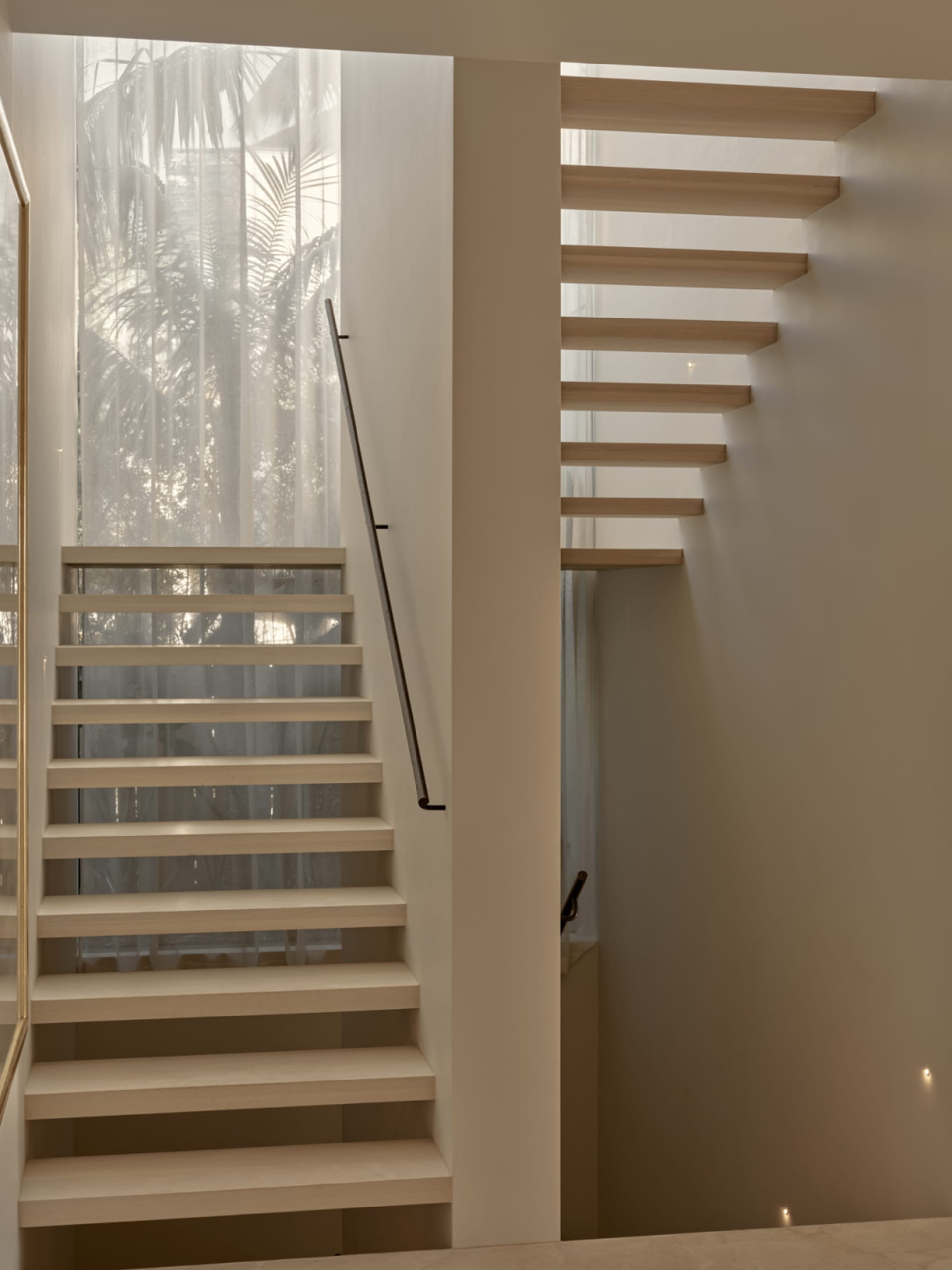A well-lit interior staircase with two sets of stairs, one on each side, in a residential home with a white color scheme and wooden stairs