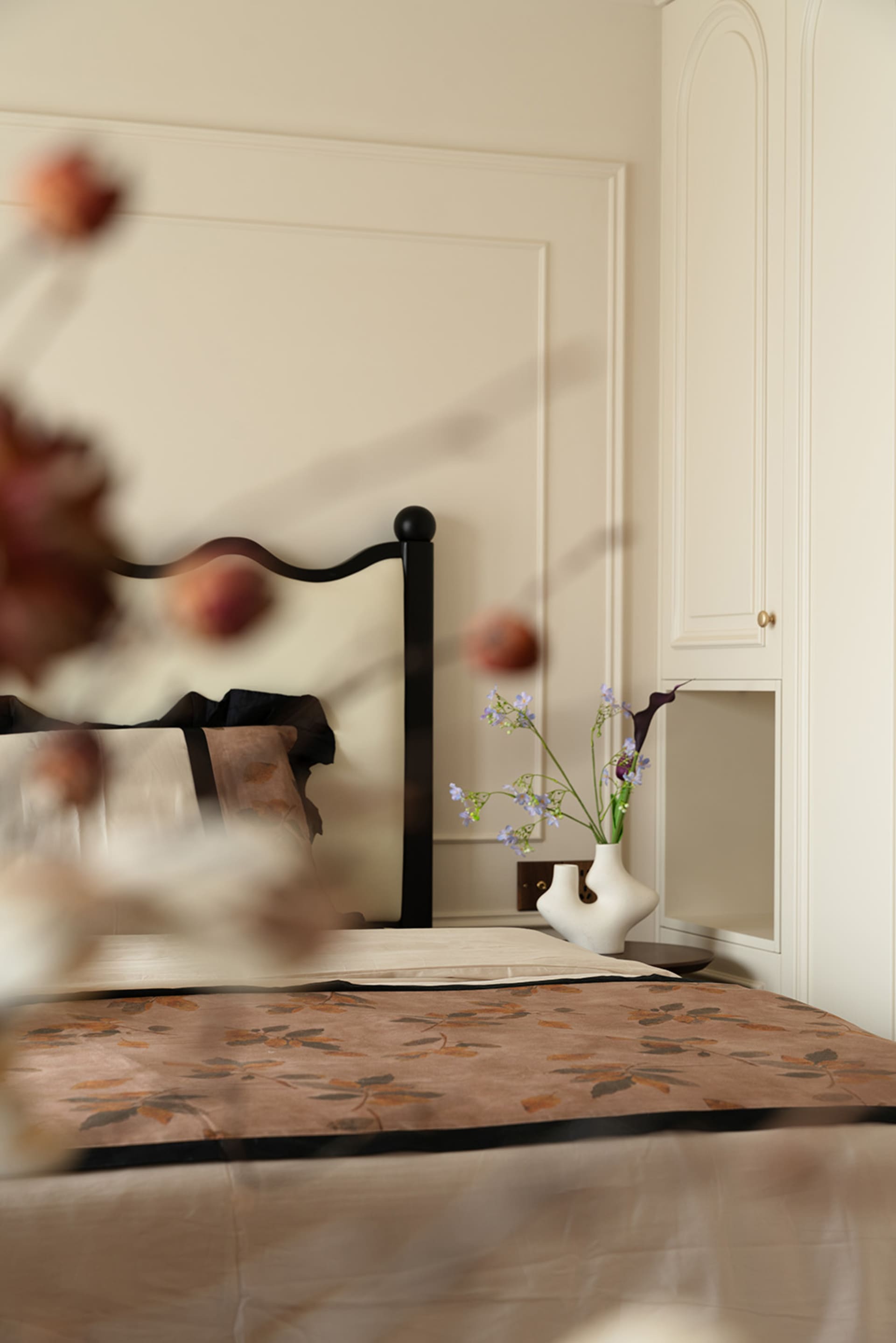 Cozy bedroom with a bed against a wall, vases, and a potted plant, creating a warm atmosphere