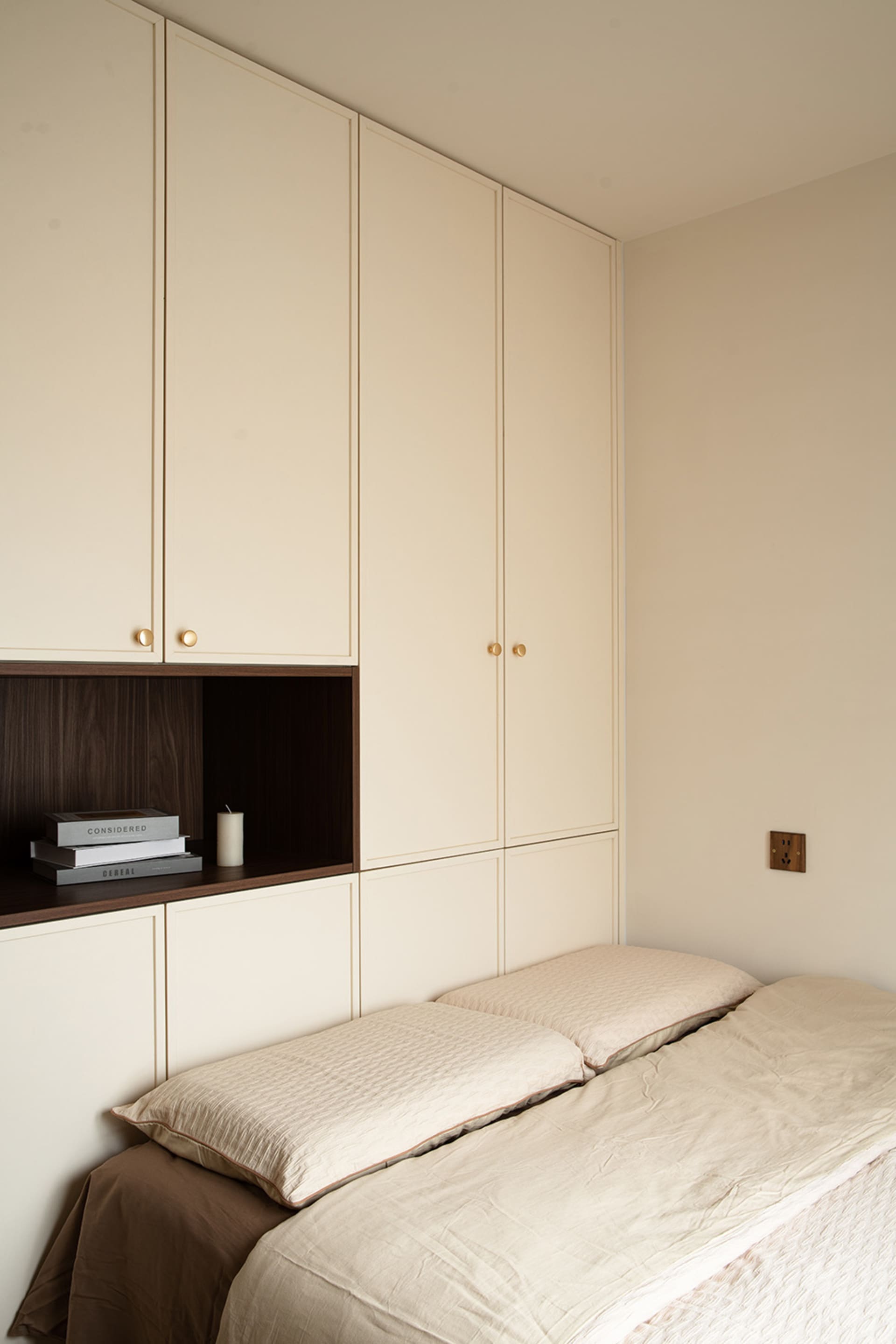 A calm and organized bedroom with two beds, a bookshelf, and a cup, featuring white walls and cabinets