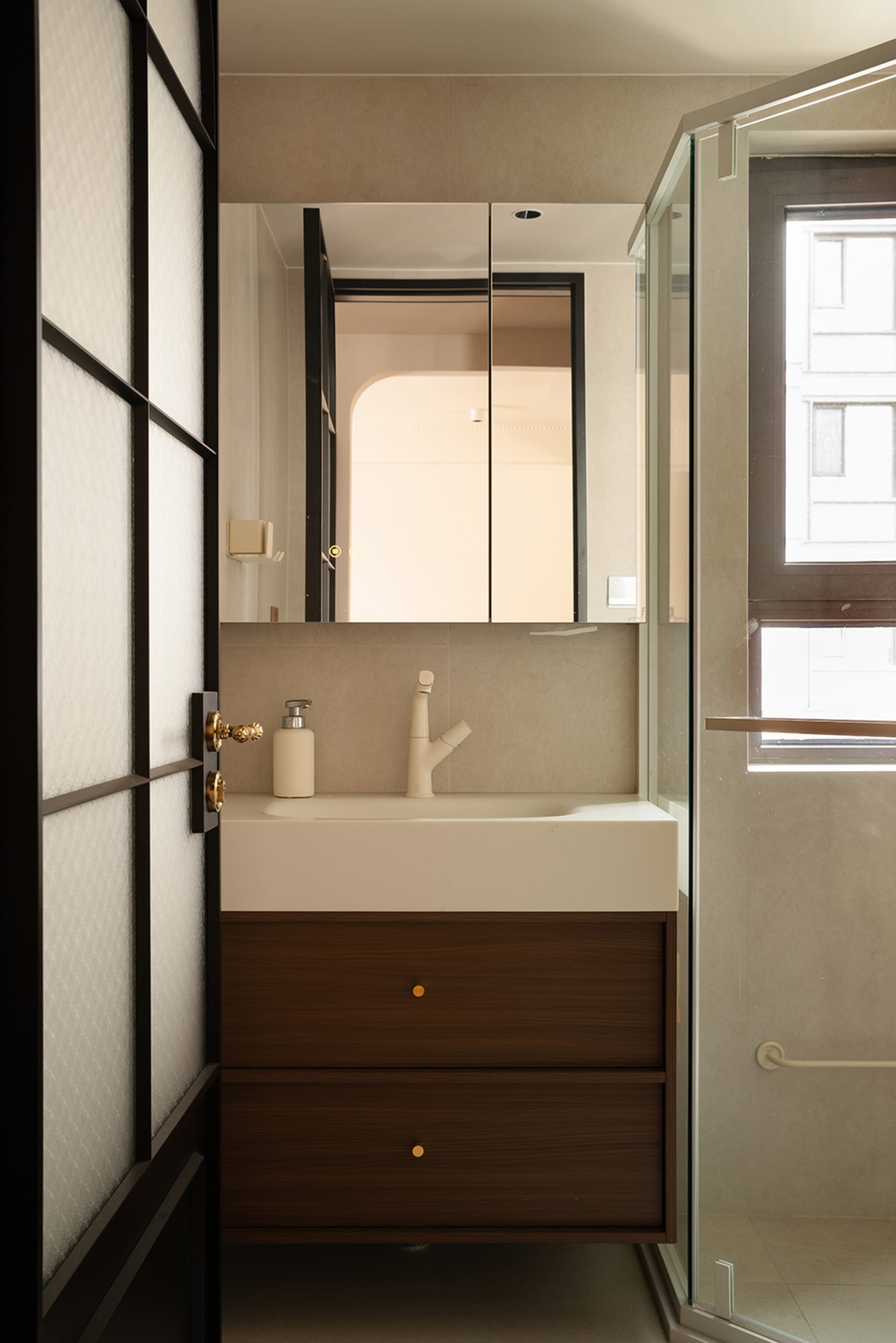Modern bathroom with a white sink, brown-framed mirror, and a shower area to the right, featuring two bottles on the countertop