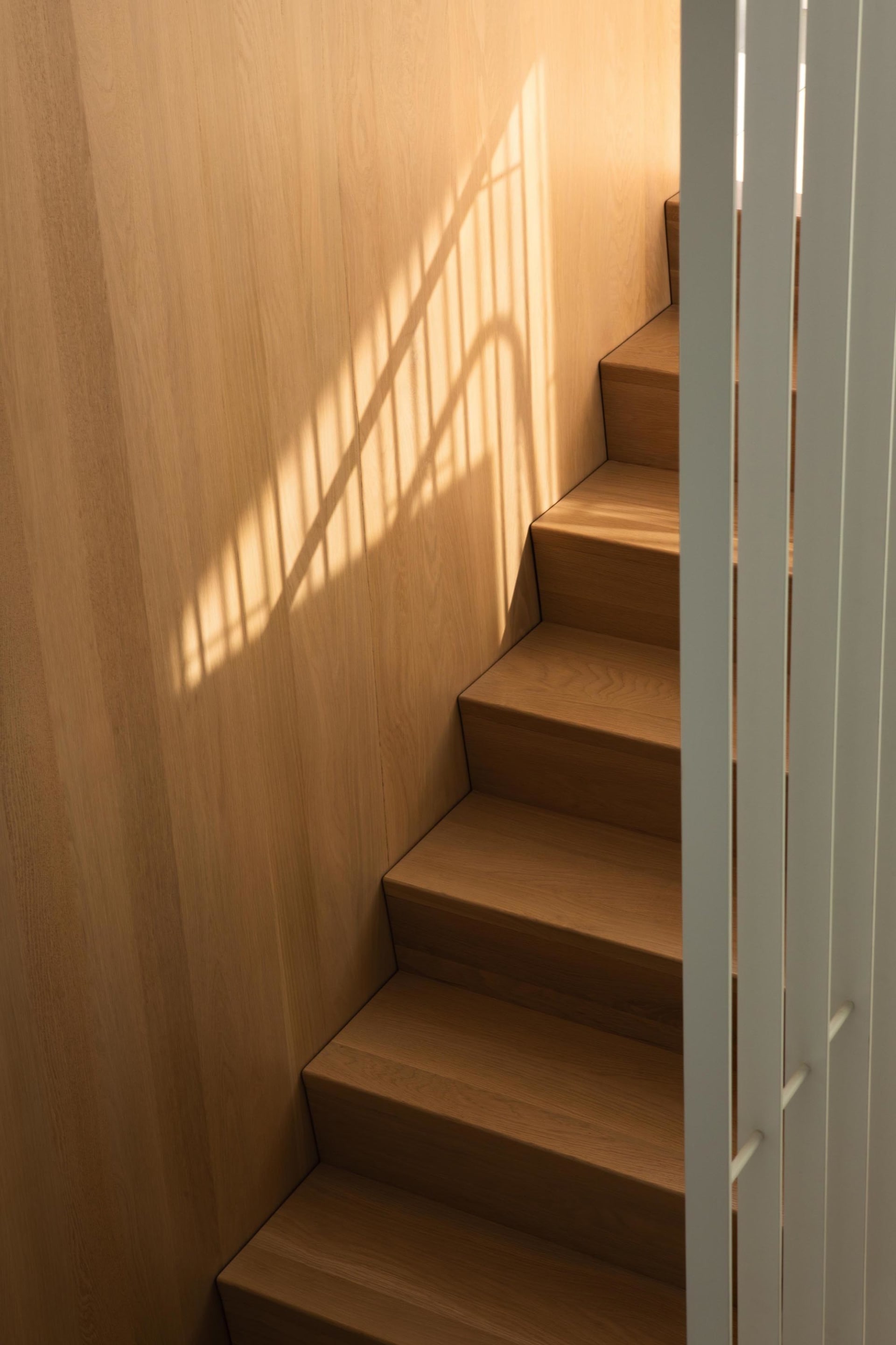 A wooden staircase with brown tones, well-lit and inviting, with a shadow on the adjacent wall