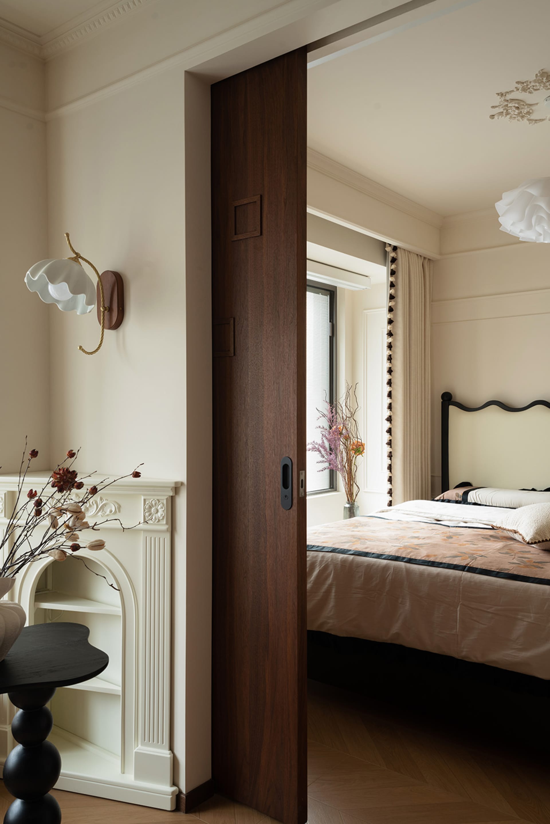 A calm bedroom with a wooden door, a large bed, two vases, and a potted plant, with natural light from the window