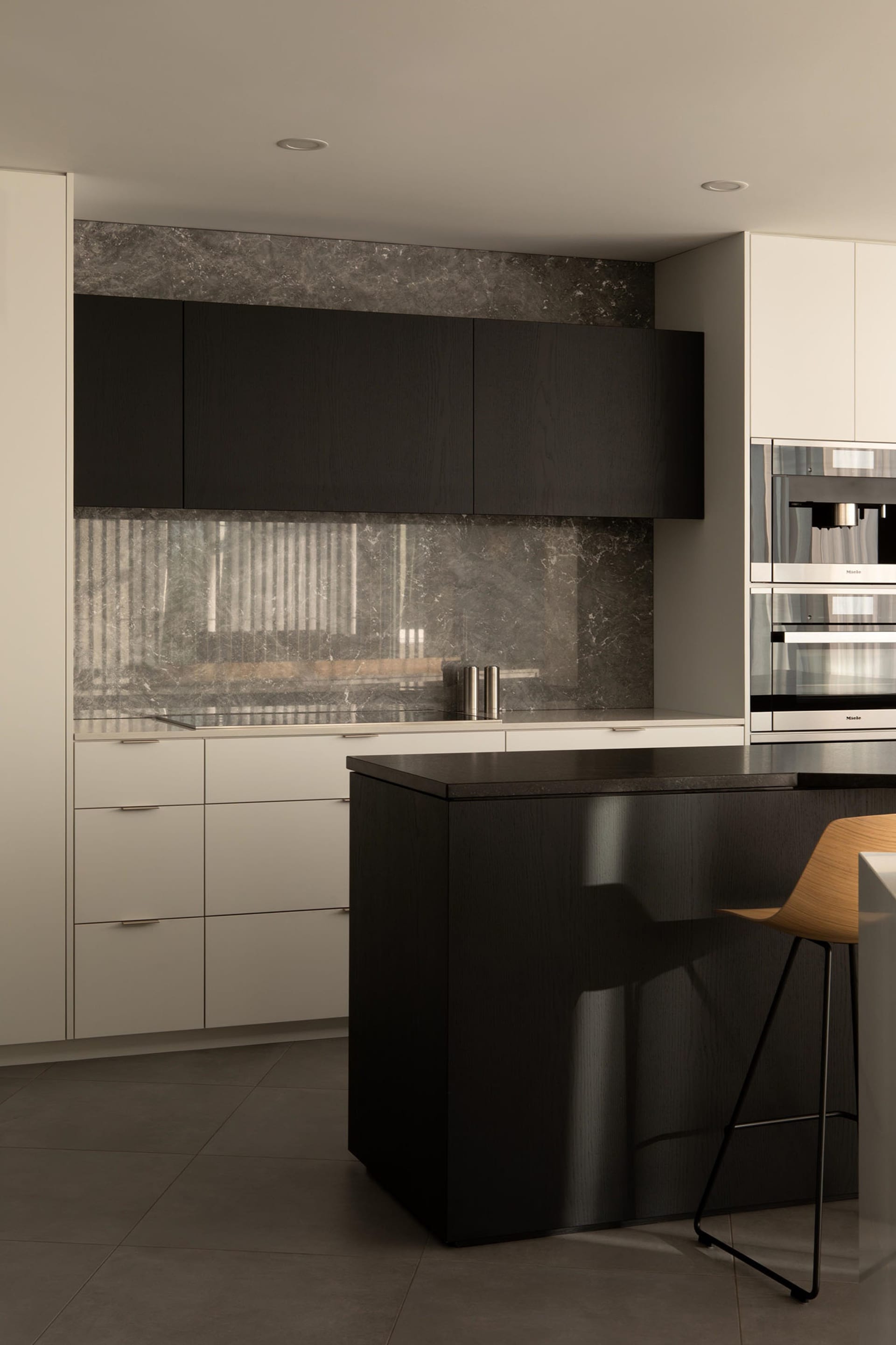 Modern kitchen with black cabinets, marble countertops, a large island, two ovens, and a sink