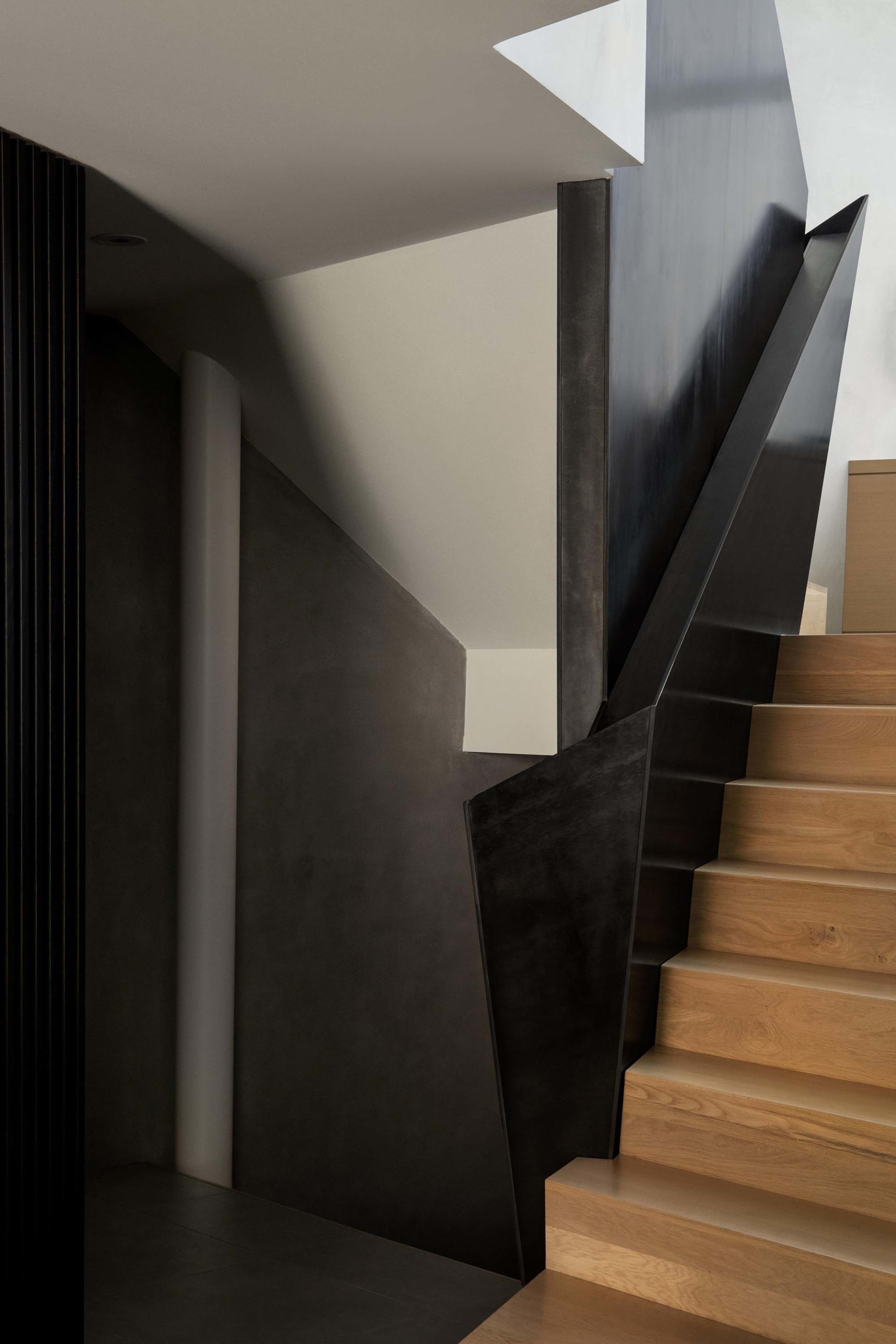 A well-lit interior staircase with wooden steps and a black railing, set against a wall in a modern home