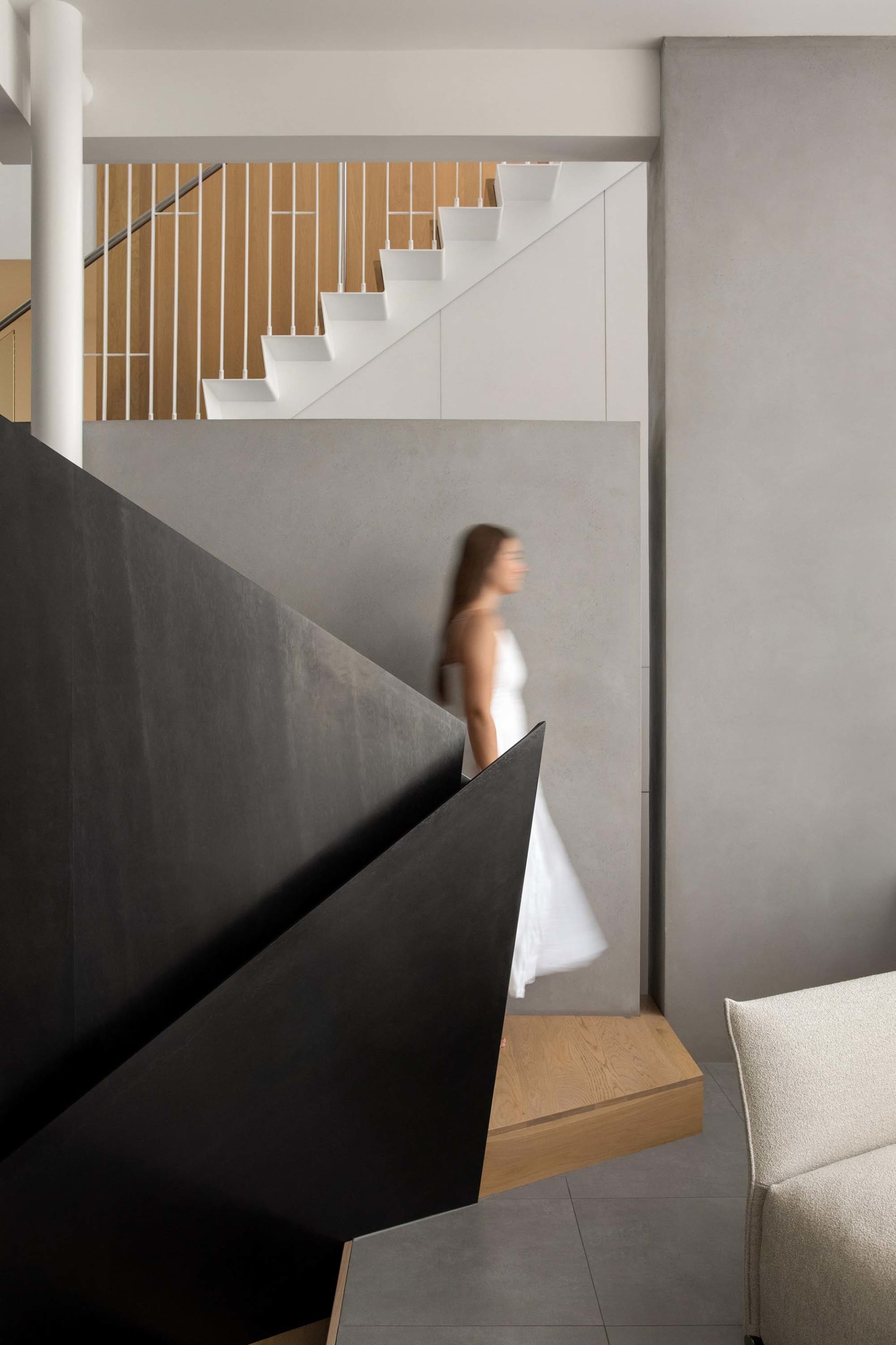 A woman in a white dress walks down a staircase with a black railing in a well-designed interior space
