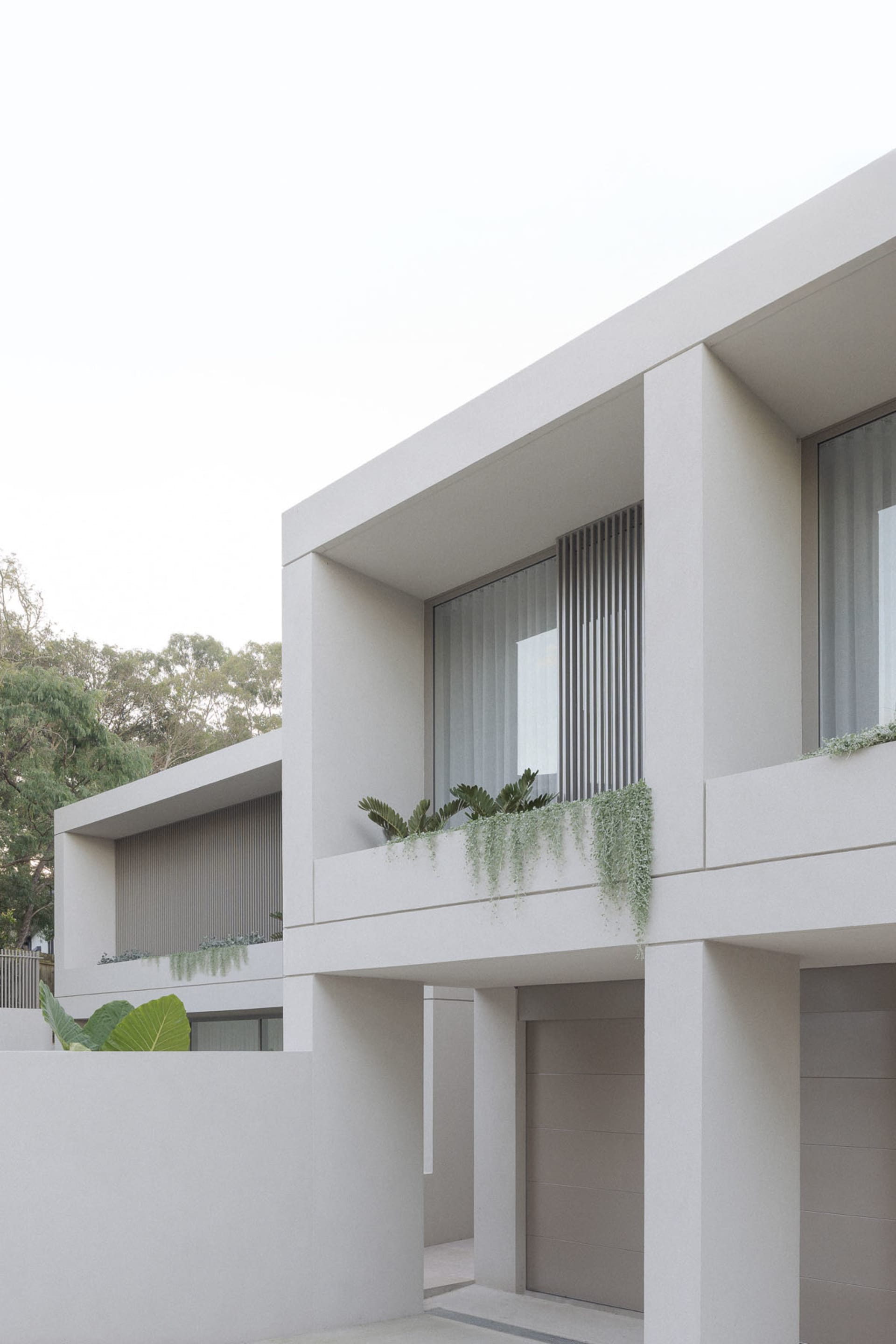 Two white buildings with large windows, one with a balcony and plants, the other with ivy-covered wall, in a calm and serene atmosphere