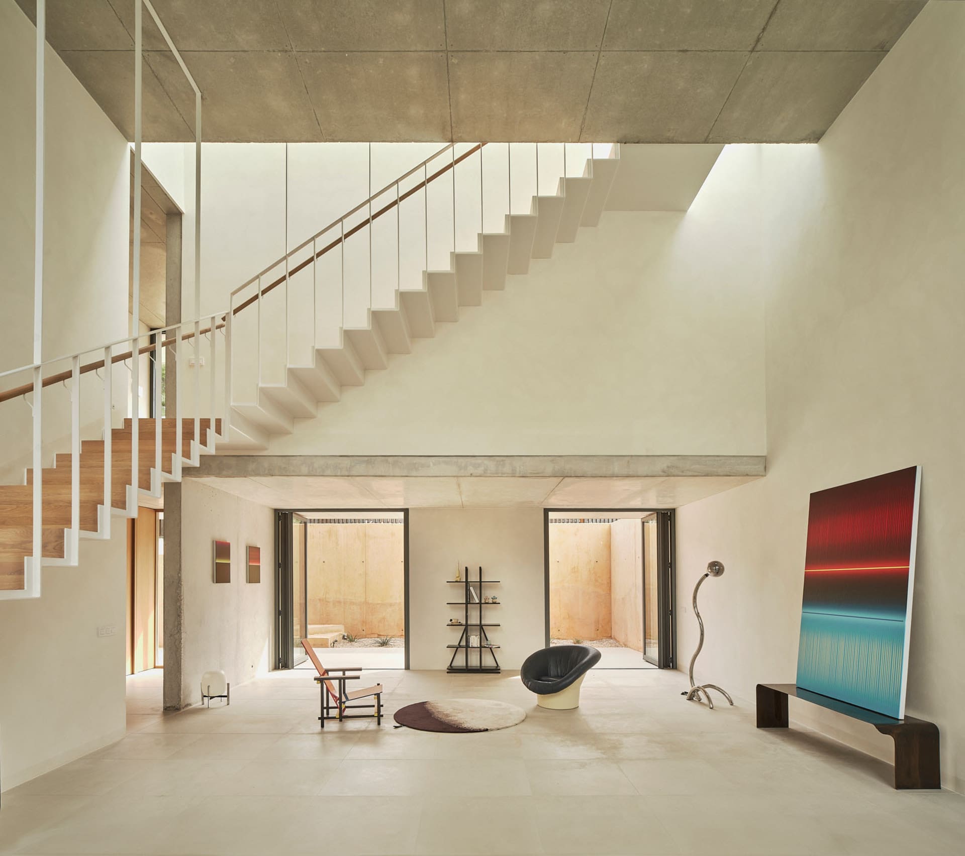 Bright and inviting open living area with a white staircase, minimalist design, two chairs, a couch, and natural light from windows