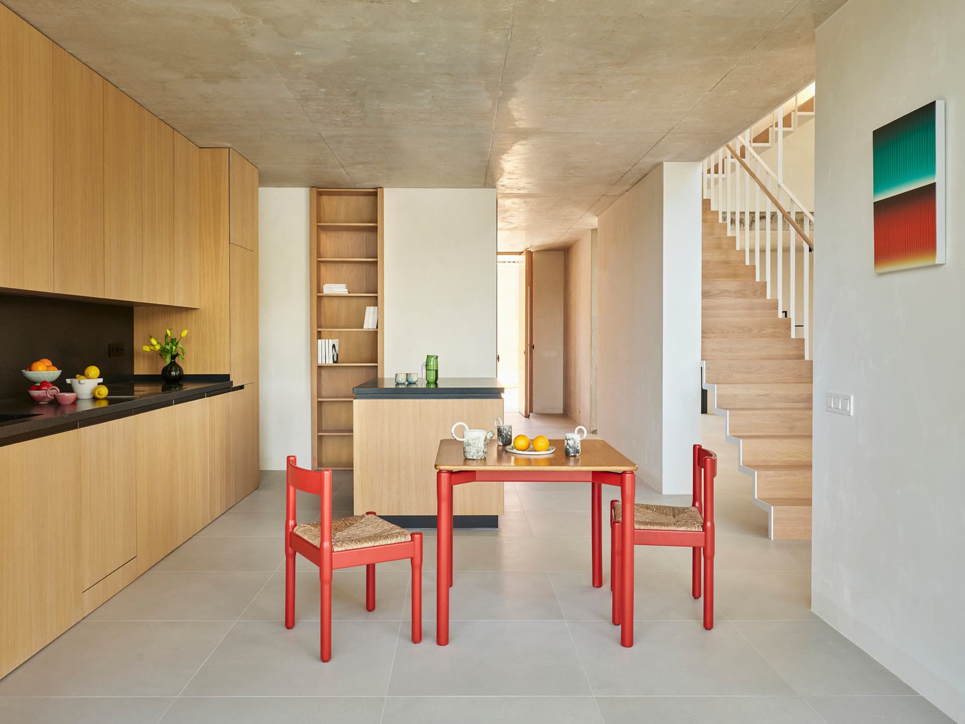 Modern kitchen and dining area with wooden cabinets, red chairs, and a cozy atmosphere, featuring a main dining table and a smaller table nearby