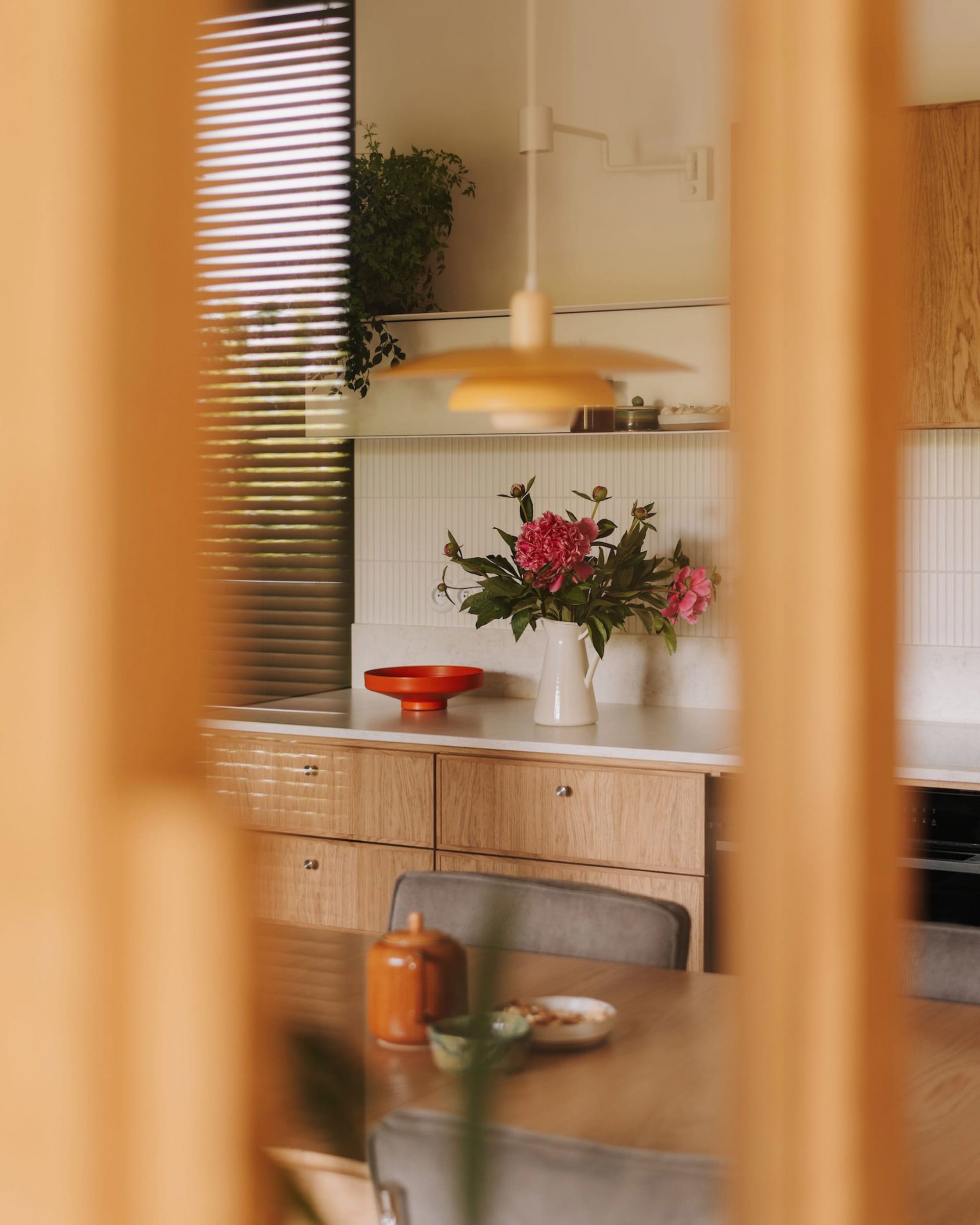 Warm kitchen with wooden cabinets and countertops, featuring a vase, bowl, cup, and potted plants, creating a cozy atmosphere