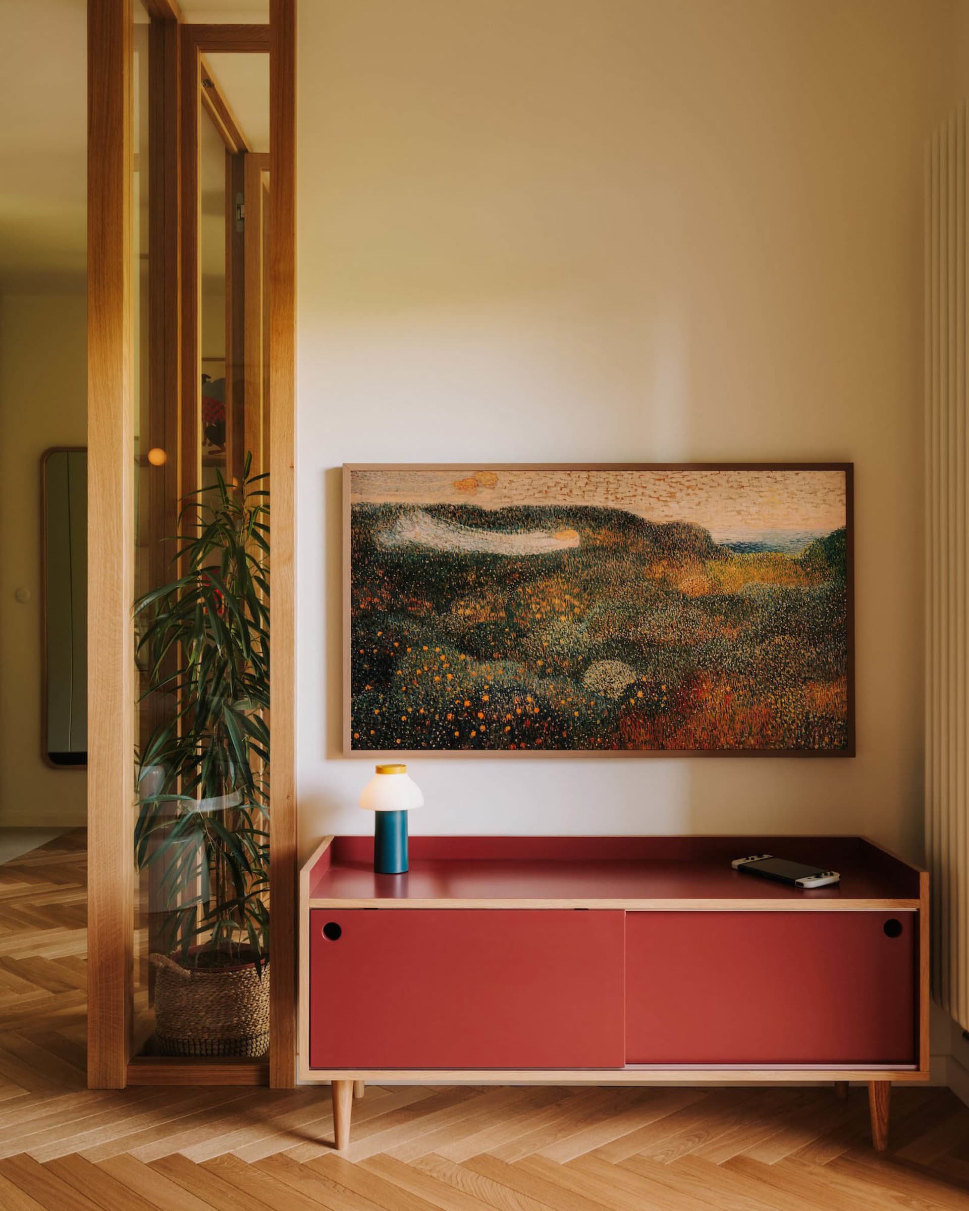 A warm and inviting living area with a red cabinet, potted plants, and a painting on the wall, creating a cozy ambiance