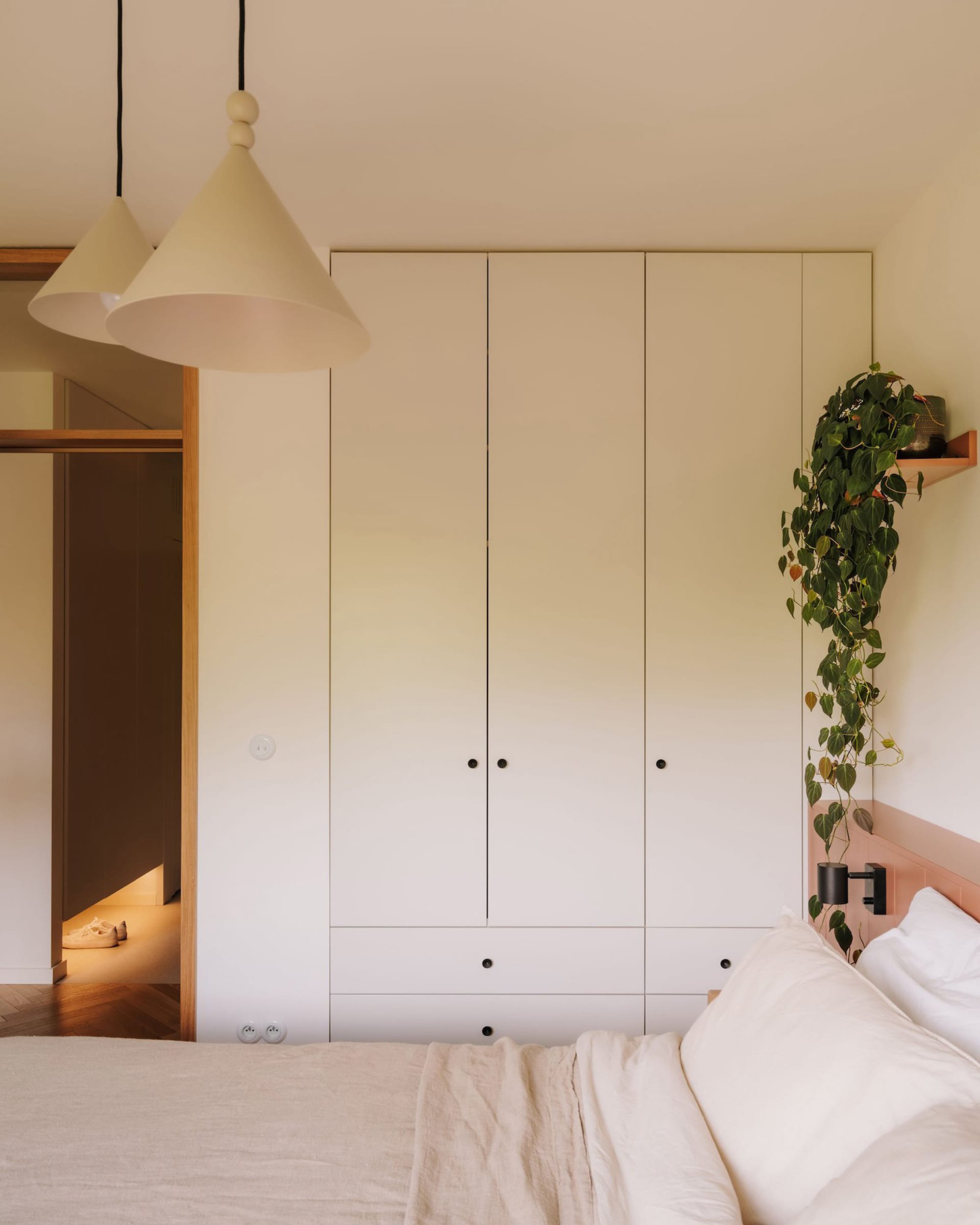 Cozy bedroom with a white bed, wooden headboard, two lamps, a closet, and a potted plant