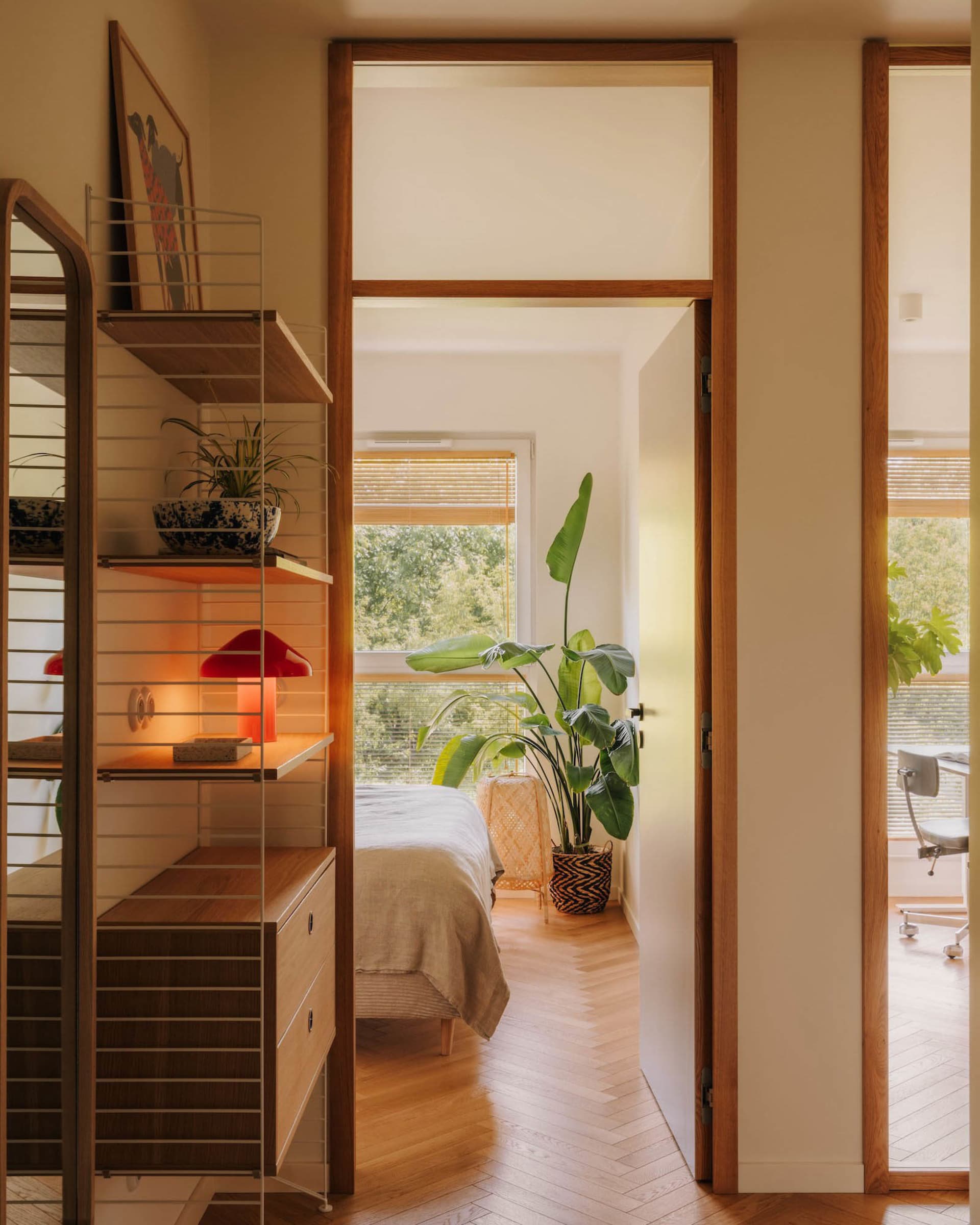 Cozy bedroom with a bed near a window, potted plants, a chair, and a book on a nearby surface