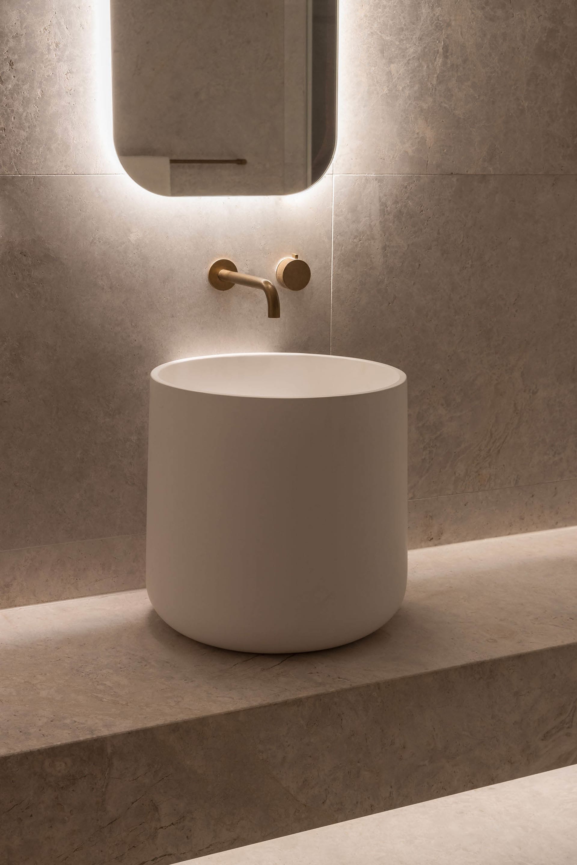 Modern bathroom with a marble bathtub, stone countertop, and a mirror above the sink area