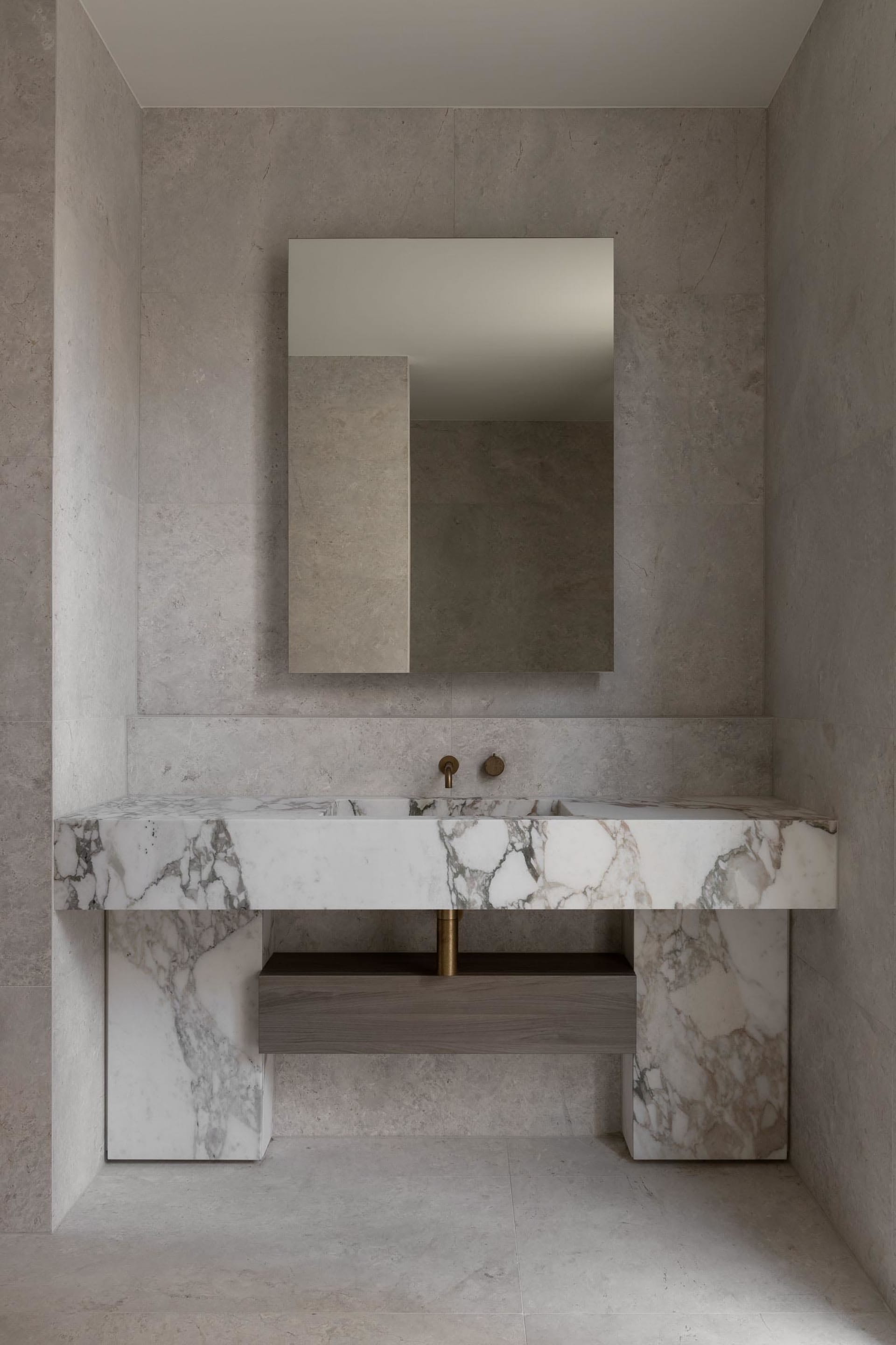 Bathroom with a marble sink area, mirror, and two faucets, giving off an elegant and luxurious vibe