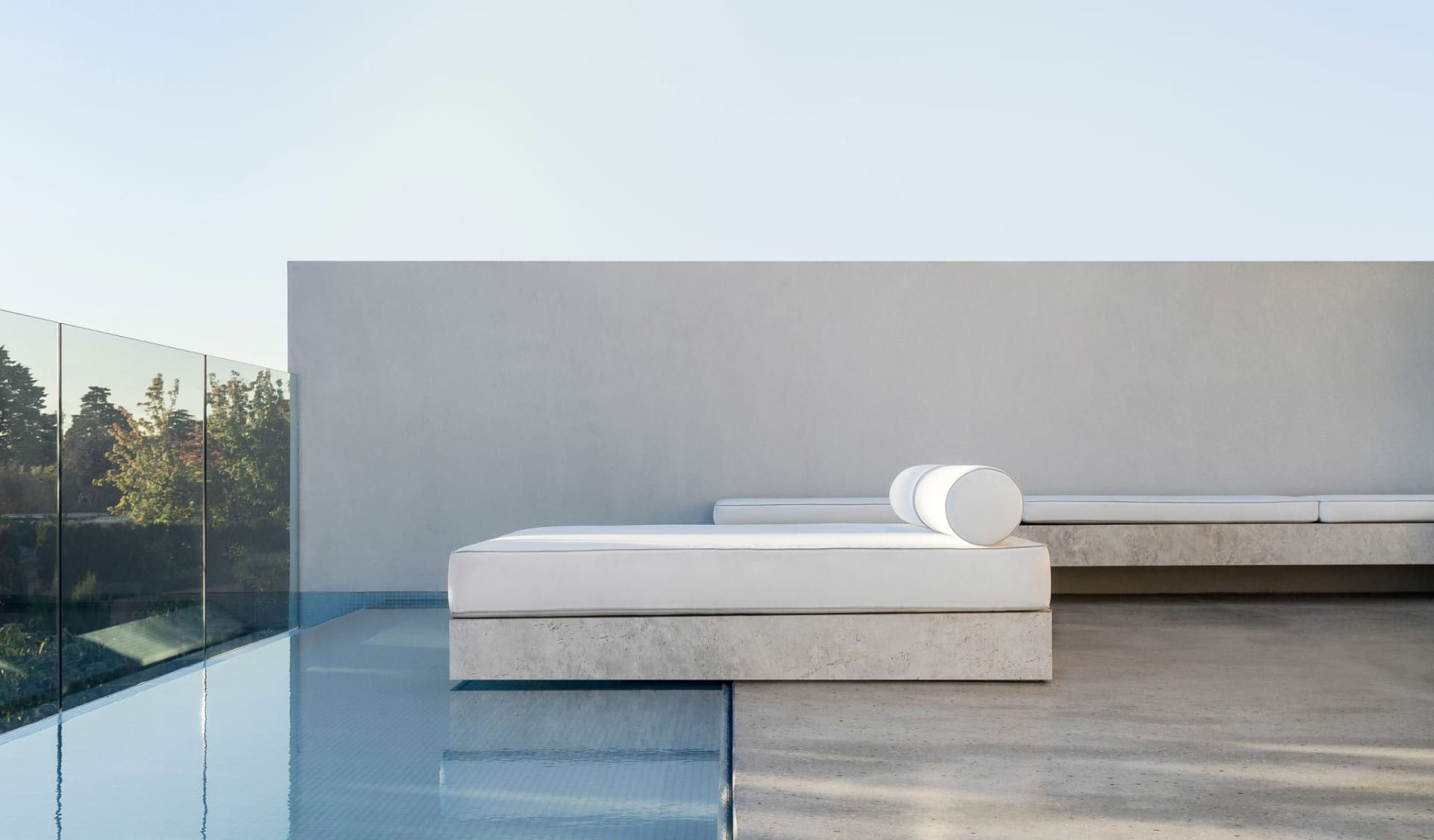 A modern outdoor patio with a large concrete sofa, two benches, and a wall, creating a relaxing and comfortable living space