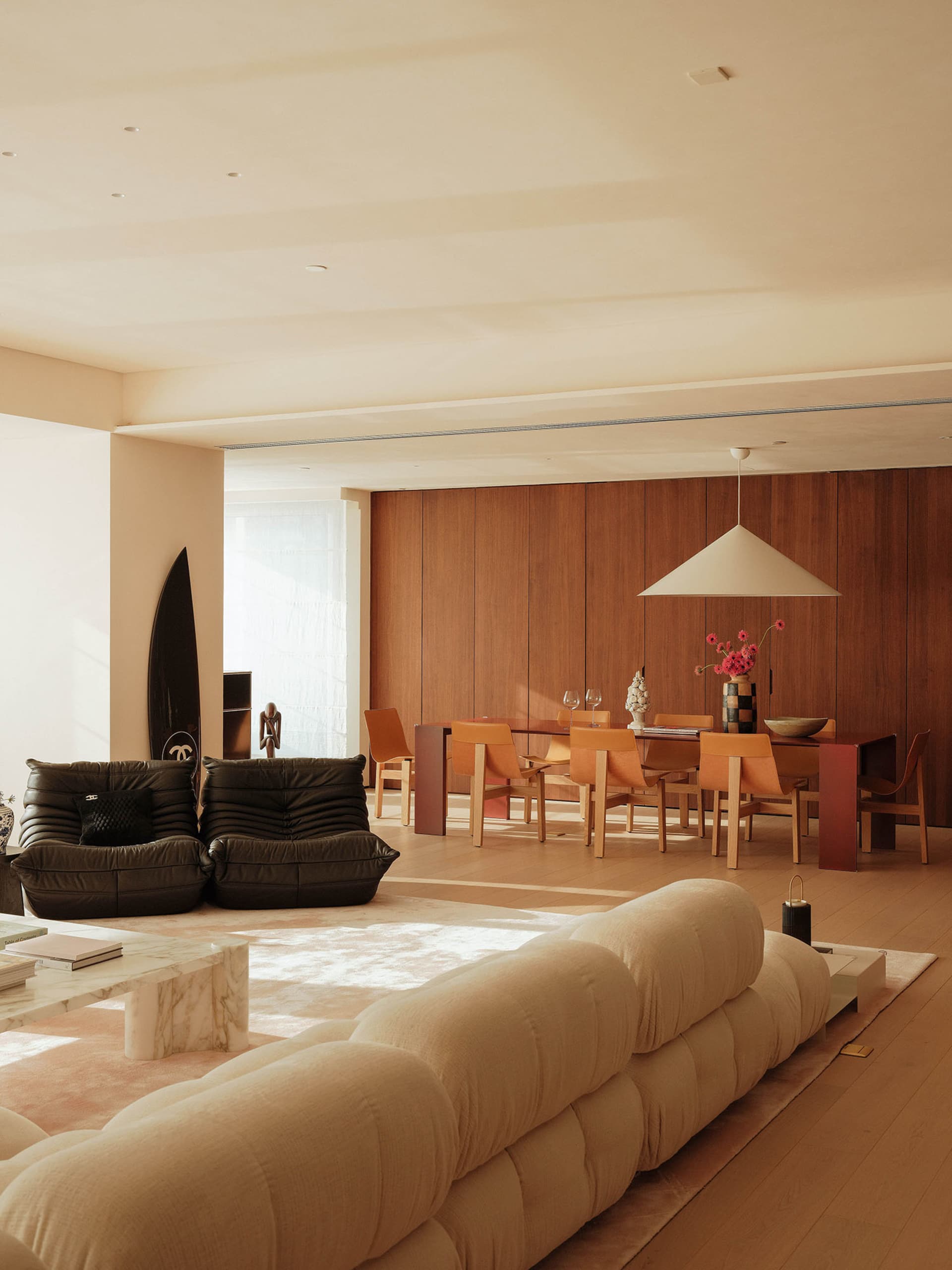 Modern living room with hardwood floors, white walls, two couches, chairs, a dining table, and decorative items
