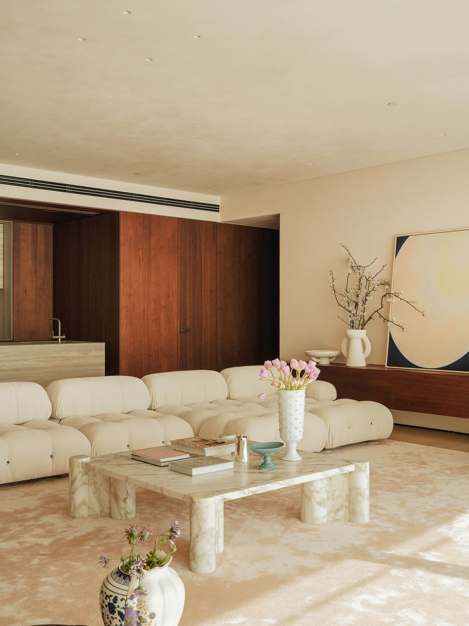 A cozy living area with a white couch, carpeted floor, chairs, a dining table, vases, and a potted plant