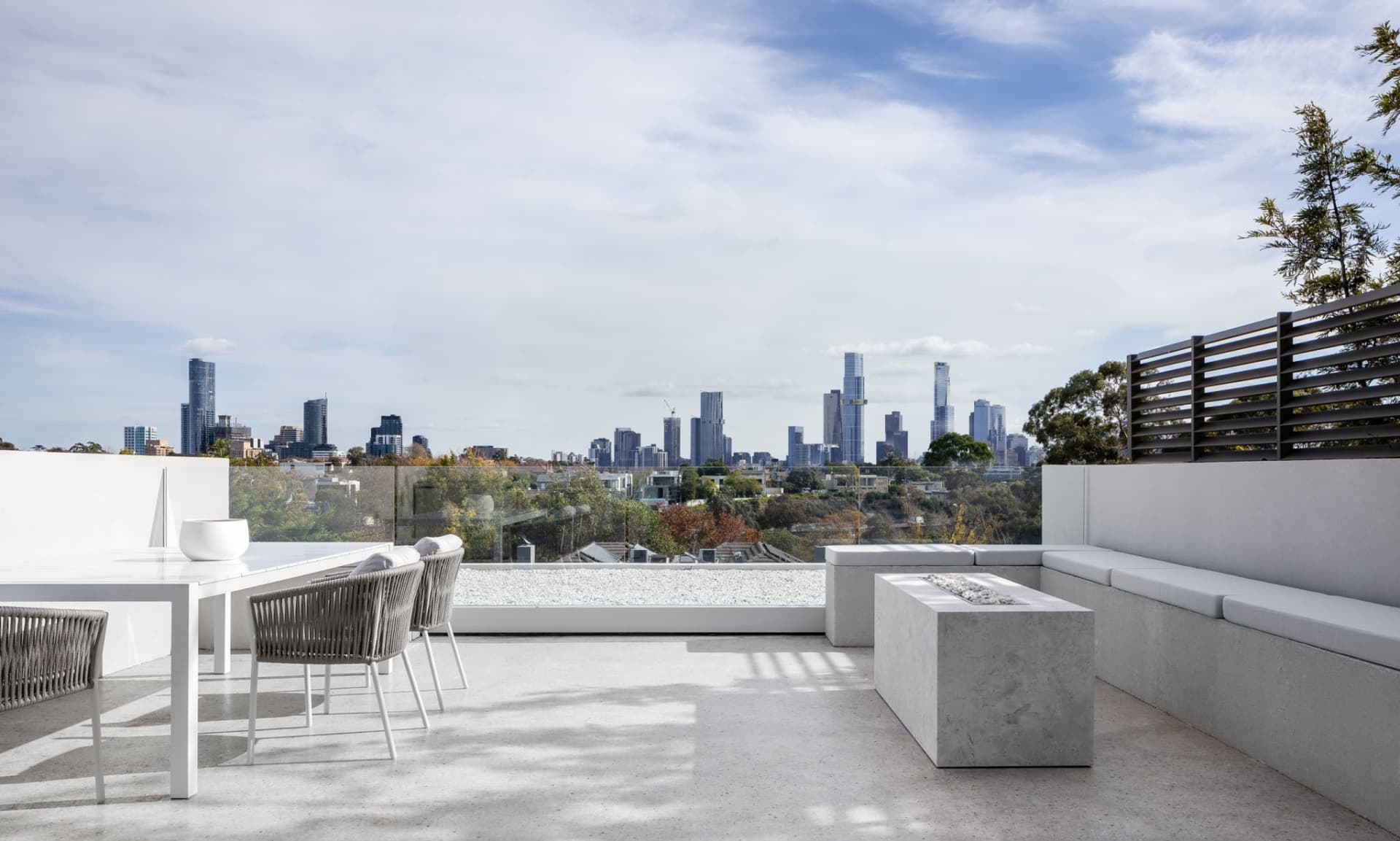 A modern living space with a glass wall offering a city skyline view, featuring two couches, a dining table, and a chair, with a stylish and functional interior design