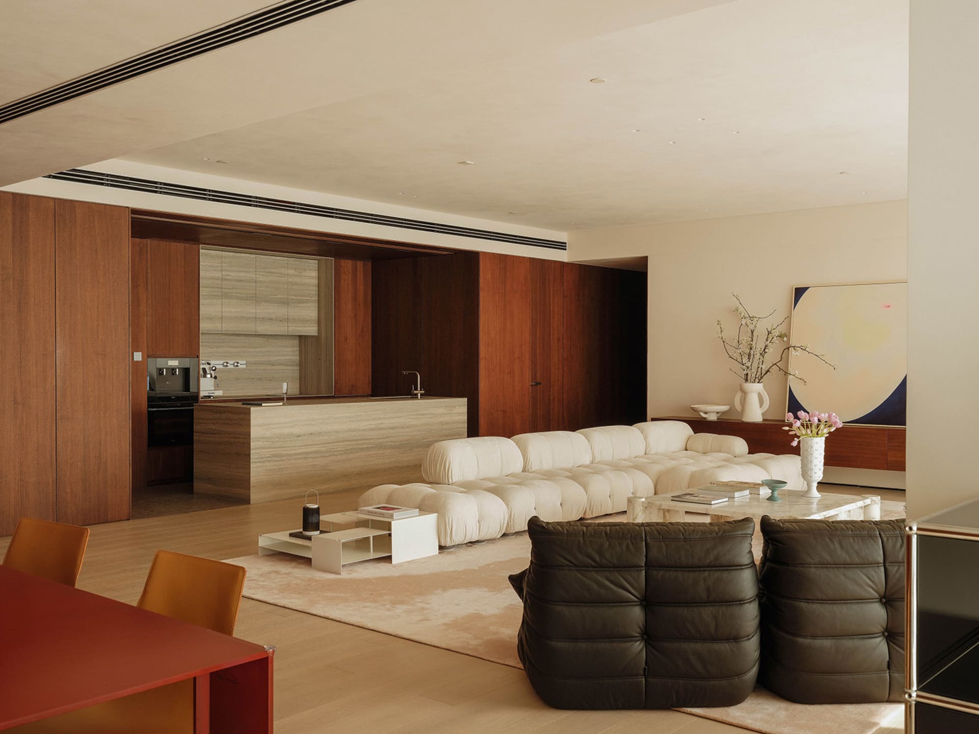 Open modern living area with a white couch, dining table, chairs, vases, potted plant, kitchenette, and refrigerator