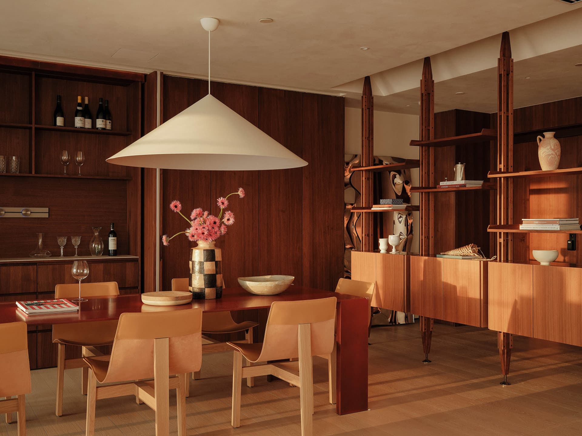 A modern dining room with a wooden table, chairs, wine glasses, and decorative vases, exuding comfort and luxury