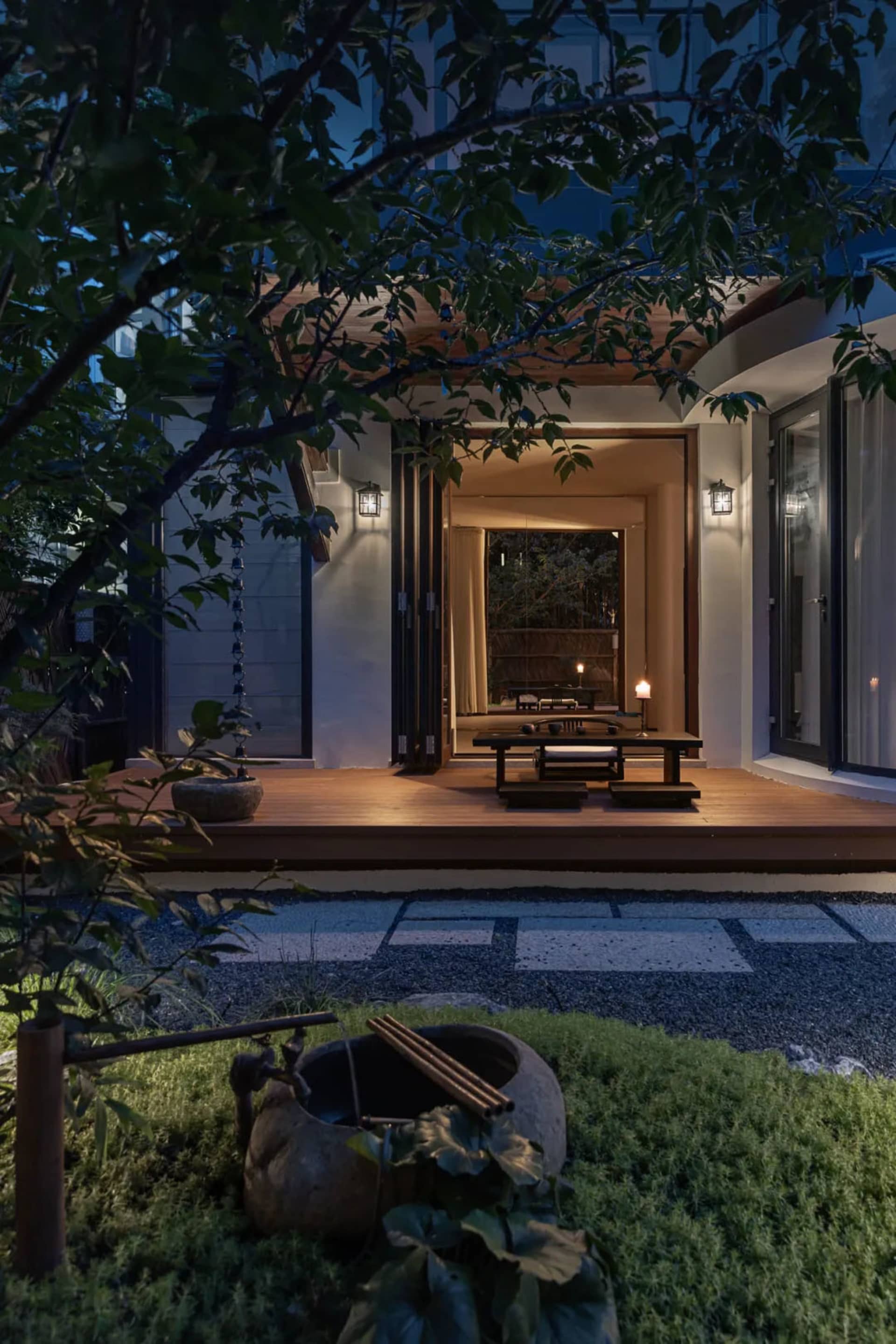 Serene Asian-style house with a wooden deck and patio area, featuring greenery, trees, and grass