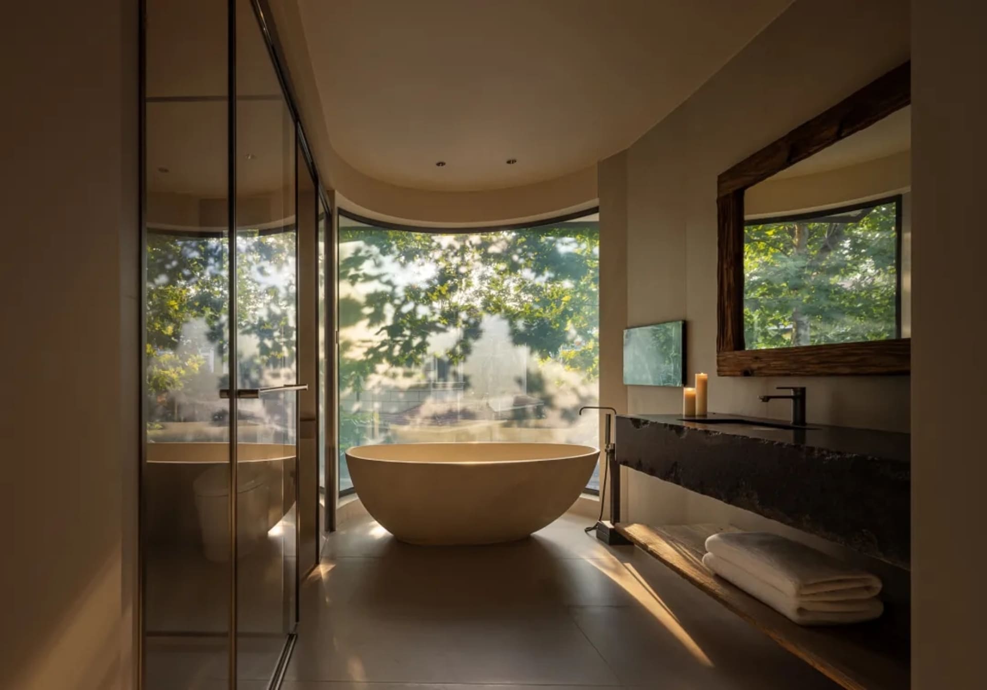 Modern bathroom with a large marble bathtub, sink, mirror, and shower area, near a window