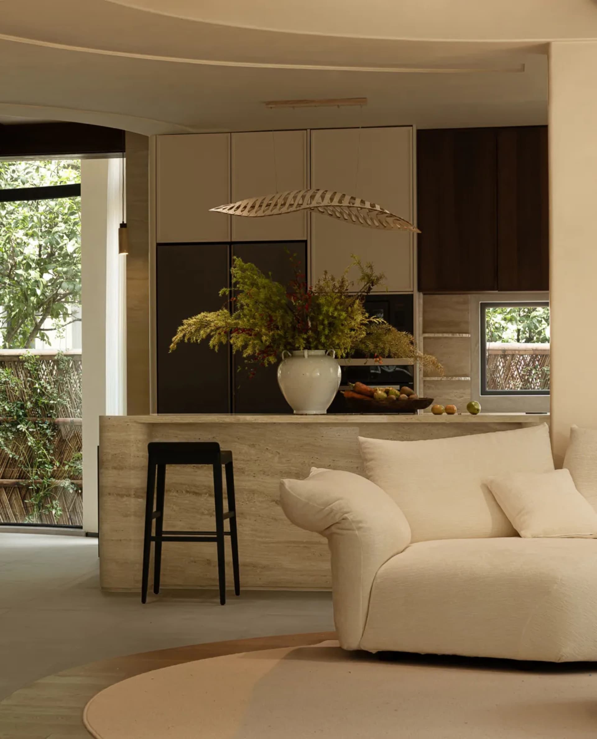 Open living area with a couch, chairs, kitchen sink, oven, and natural light from a large window