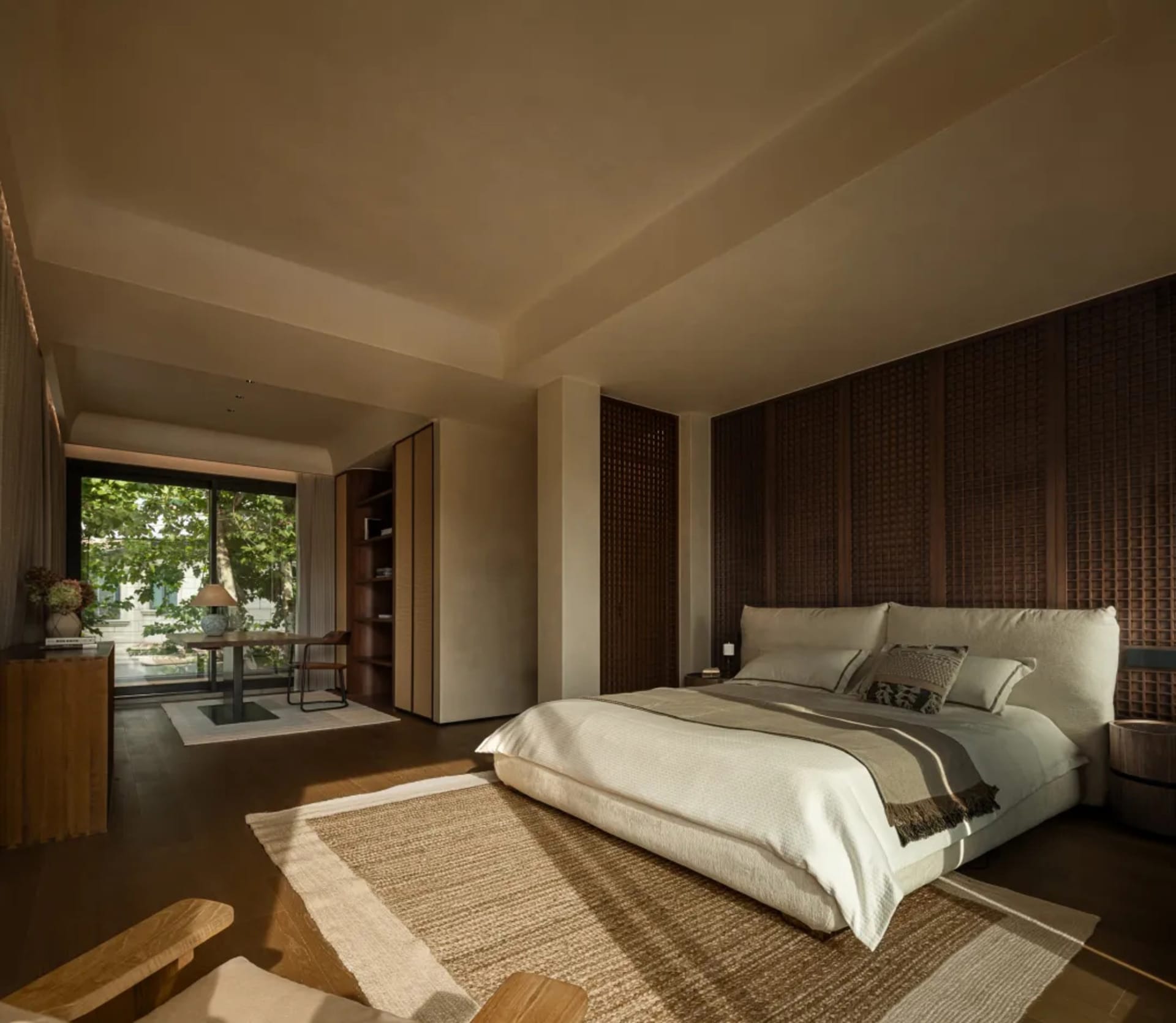 Cozy bedroom with a brown bed, two chairs, and a dining table on a hardwood floor, with a warm and inviting ambiance