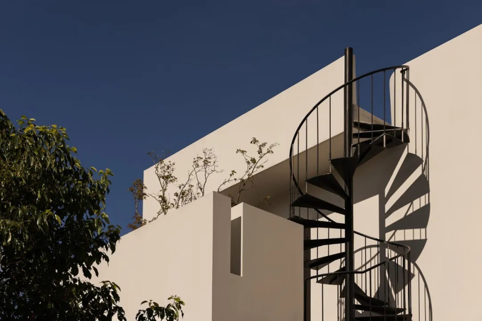 A modern building with a spiral staircase leading to a balcony, featuring a white exterior and metal stairs