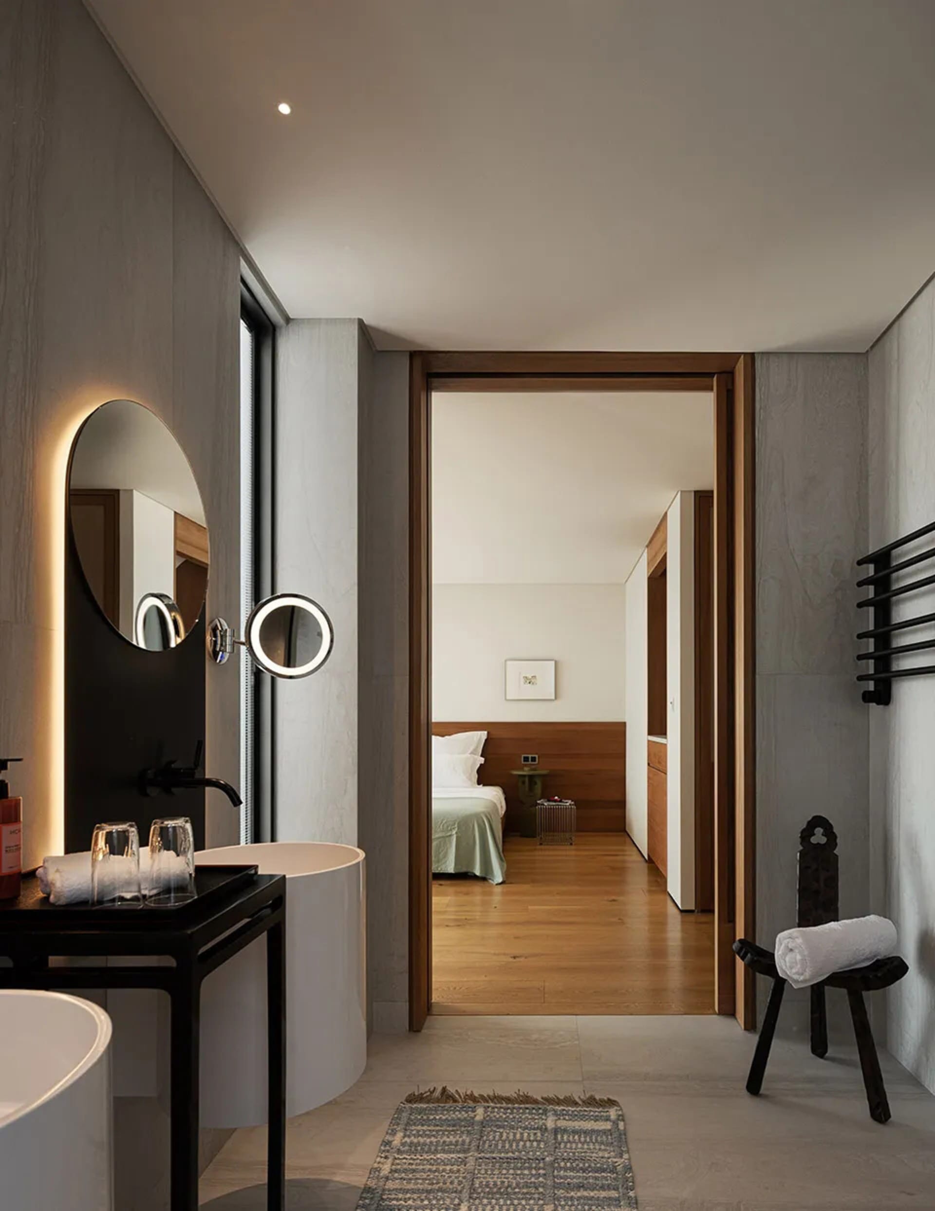 Well-lit bedroom with wooden floors and walls, featuring a large mirror, two beds, and a chair, creating a cozy and inviting atmosphere