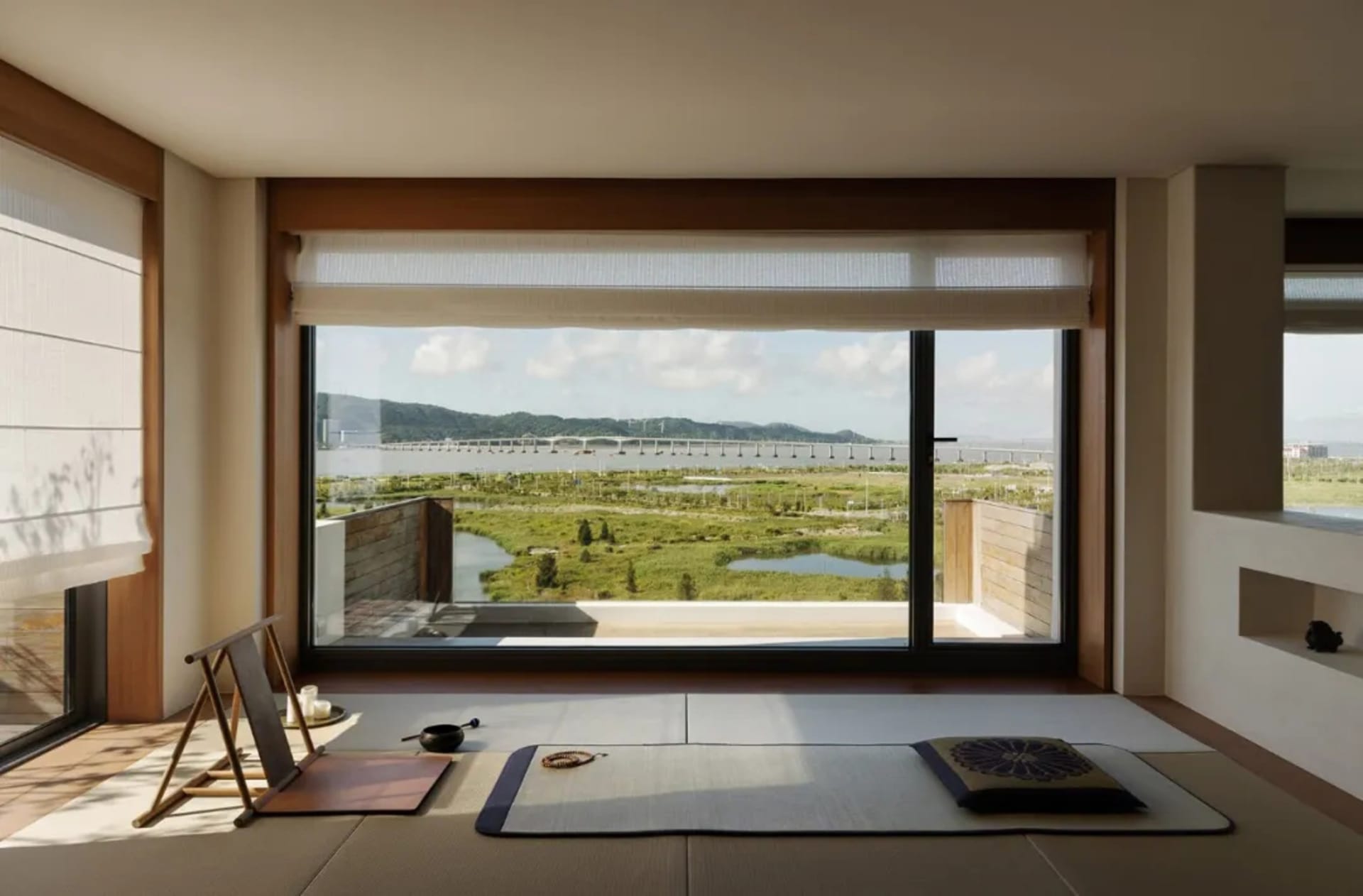 Cozy living space with a wooden floor, two couches, a chair, and a dining table, with a large window offering a scenic view of the surrounding landscape