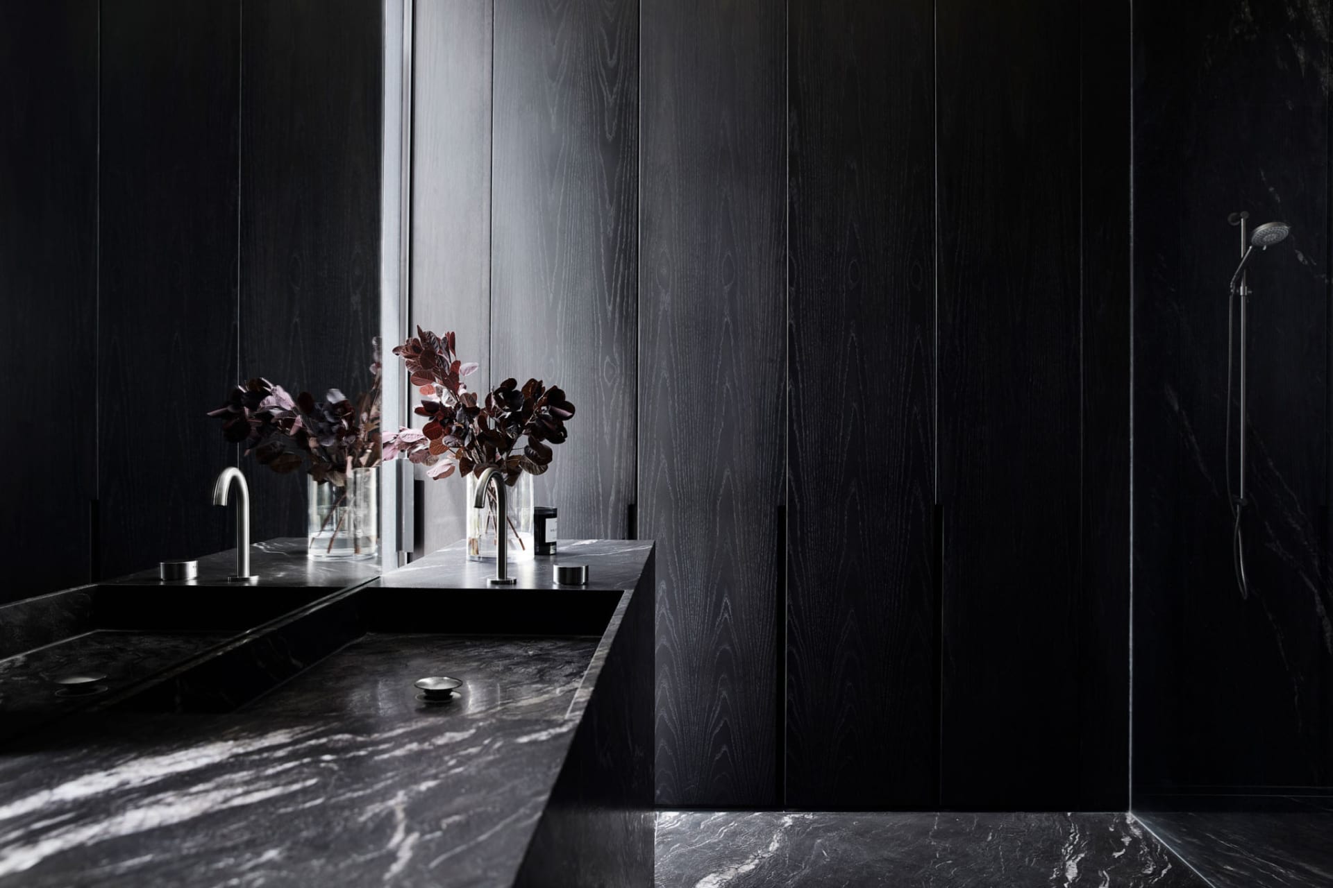 Dark and moody bathroom with a black wall, wooden countertop, and two vases on the sink area