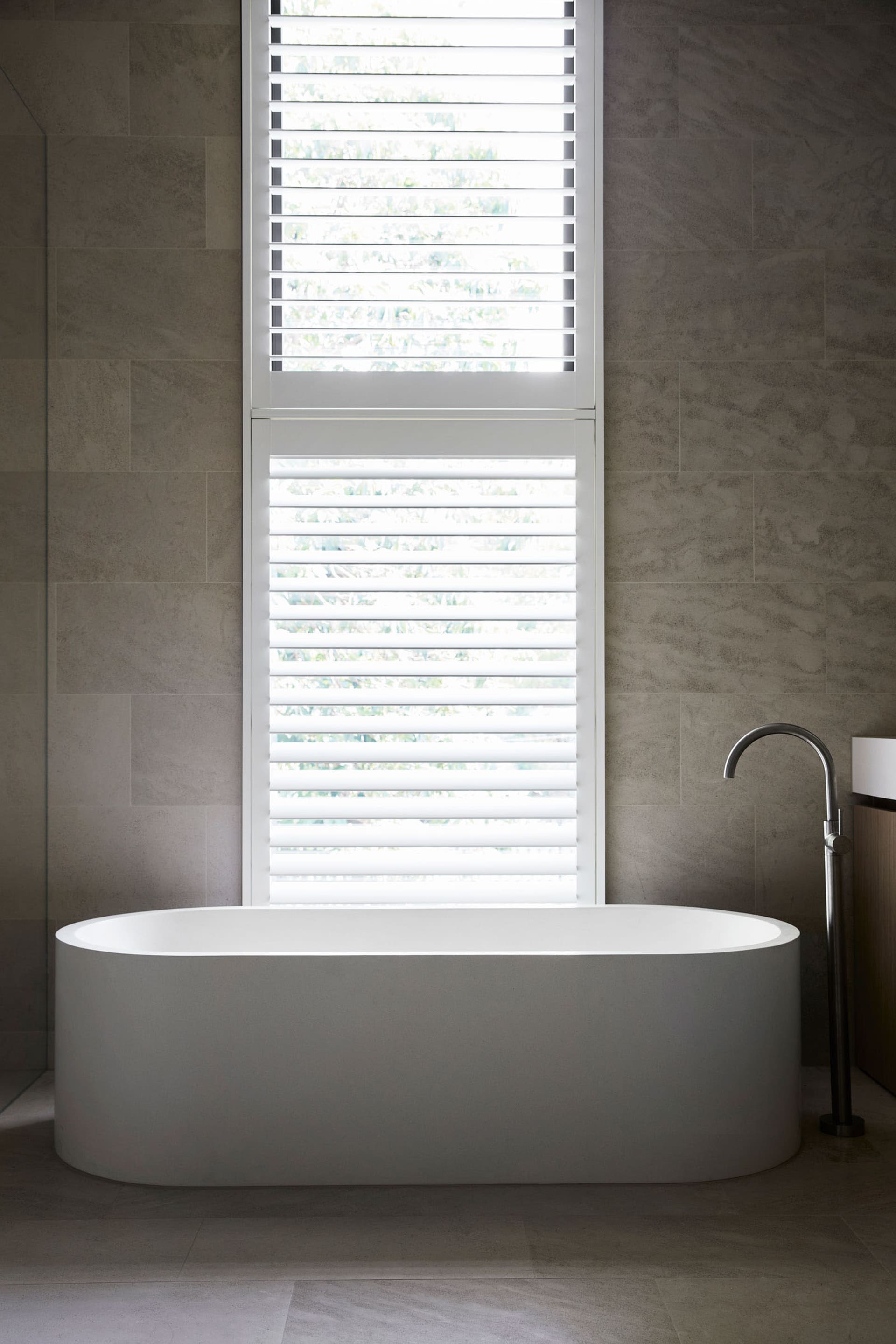 A bathroom with a white bathtub next to a window, surrounded by blinds, creating a calm and relaxing atmosphere