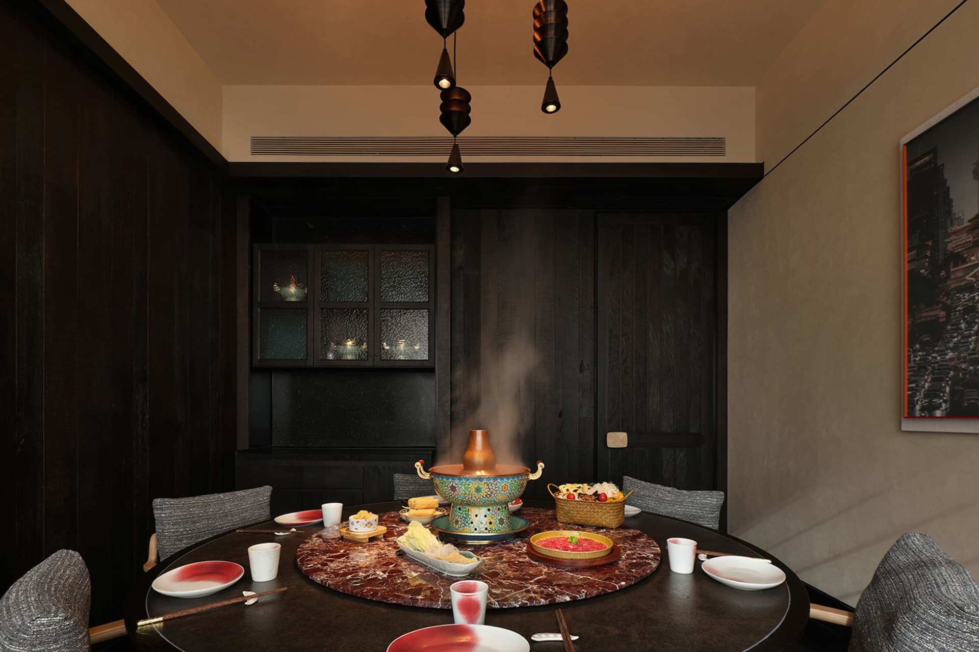 Dining room with a modern table and chairs, set with dishes and a blue vase, surrounded by a fireplace and wood and glass materials, with dim lighting creating a cozy atmosphere