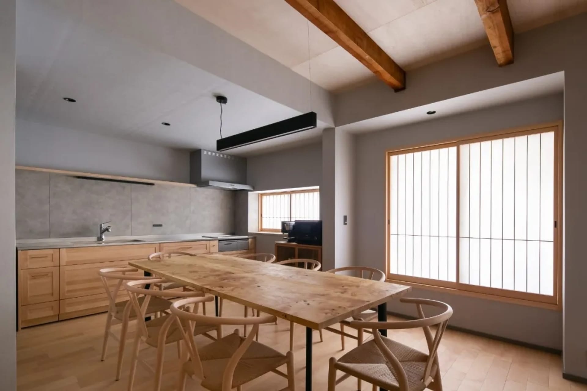 A modern kitchen and dining area with a wooden table and chairs, a refrigerator, oven, and large dining table, surrounded by natural light and sunlight