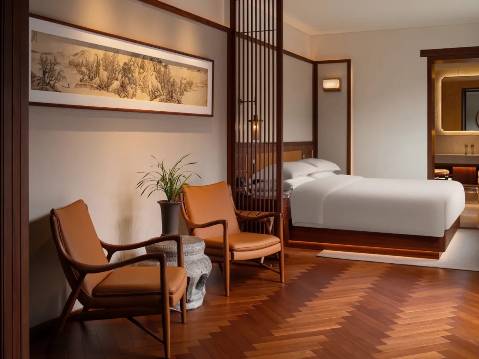 A well-lit bedroom with a bed, chair, and potted plant, featuring wood and fabric materials