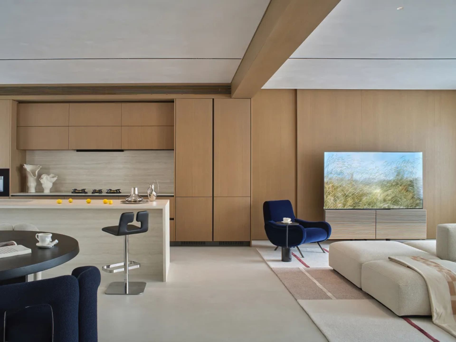 A modern living room with a large couch, chair, and dining table, decorated with wooden elements, well lit with natural light from the windows, and furnished with various items
