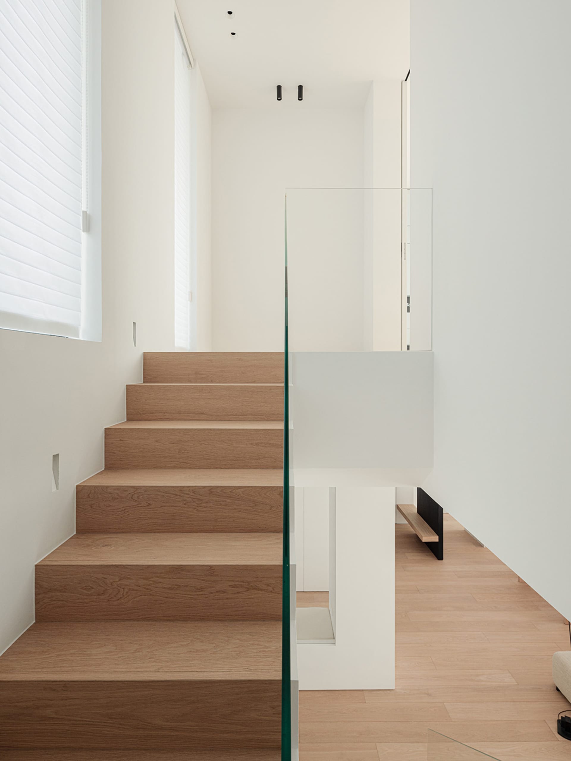 A modern staircase with wooden steps and a glass railing in a bright and airy white house