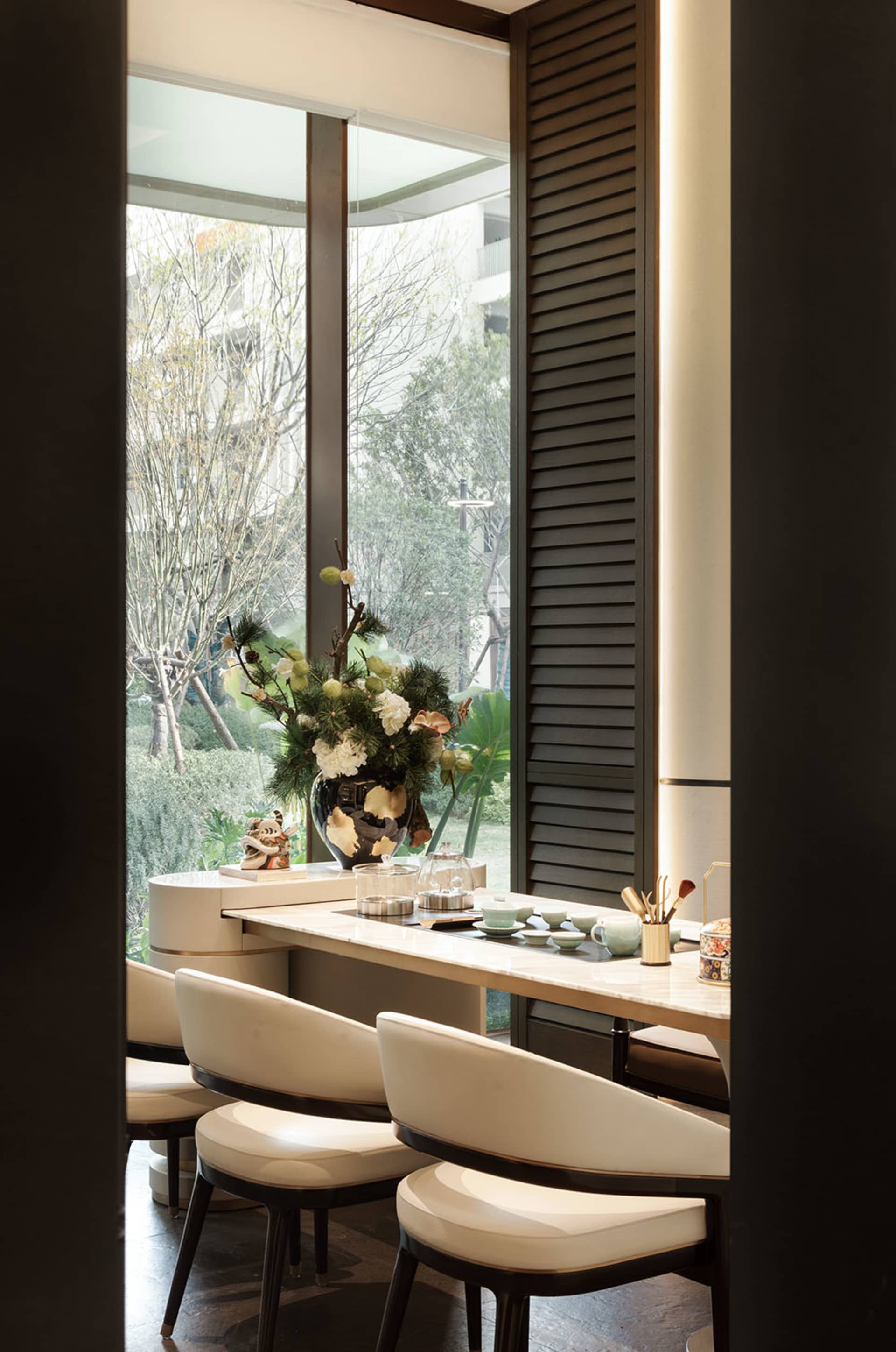 A dining room with a wooden table and chairs, a potted plant, and natural light from a window