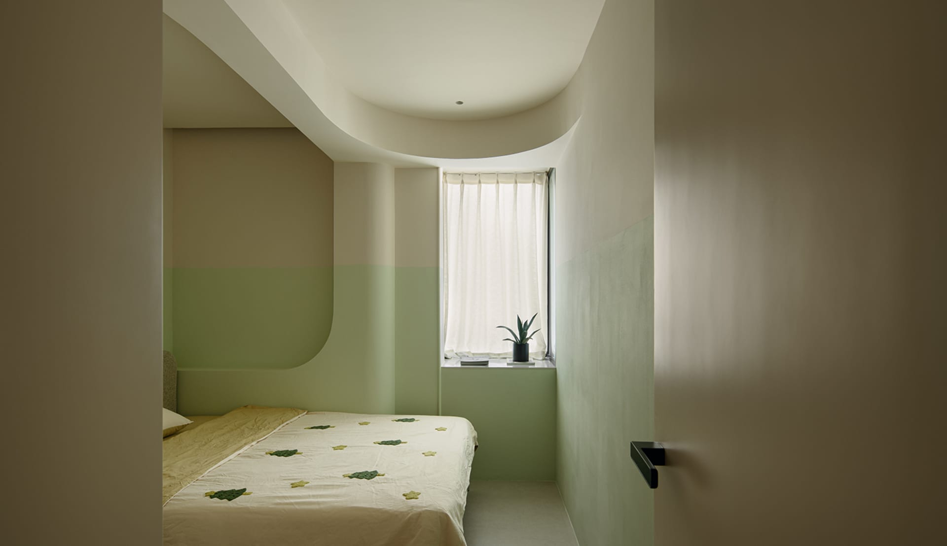 A small, cozy bedroom with a bed, window, and potted plant, featuring a green color scheme and inviting atmosphere