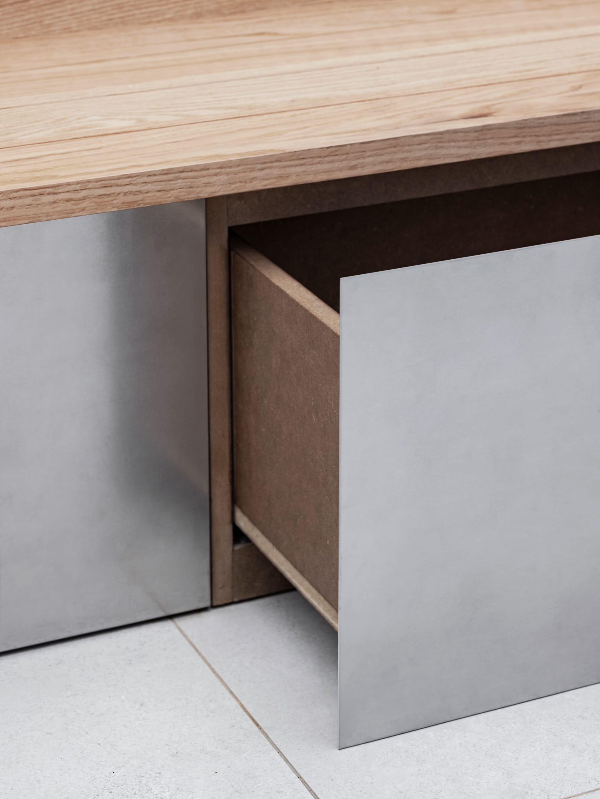 A modern dining space with a wooden table and brown drawer, set against a white floor