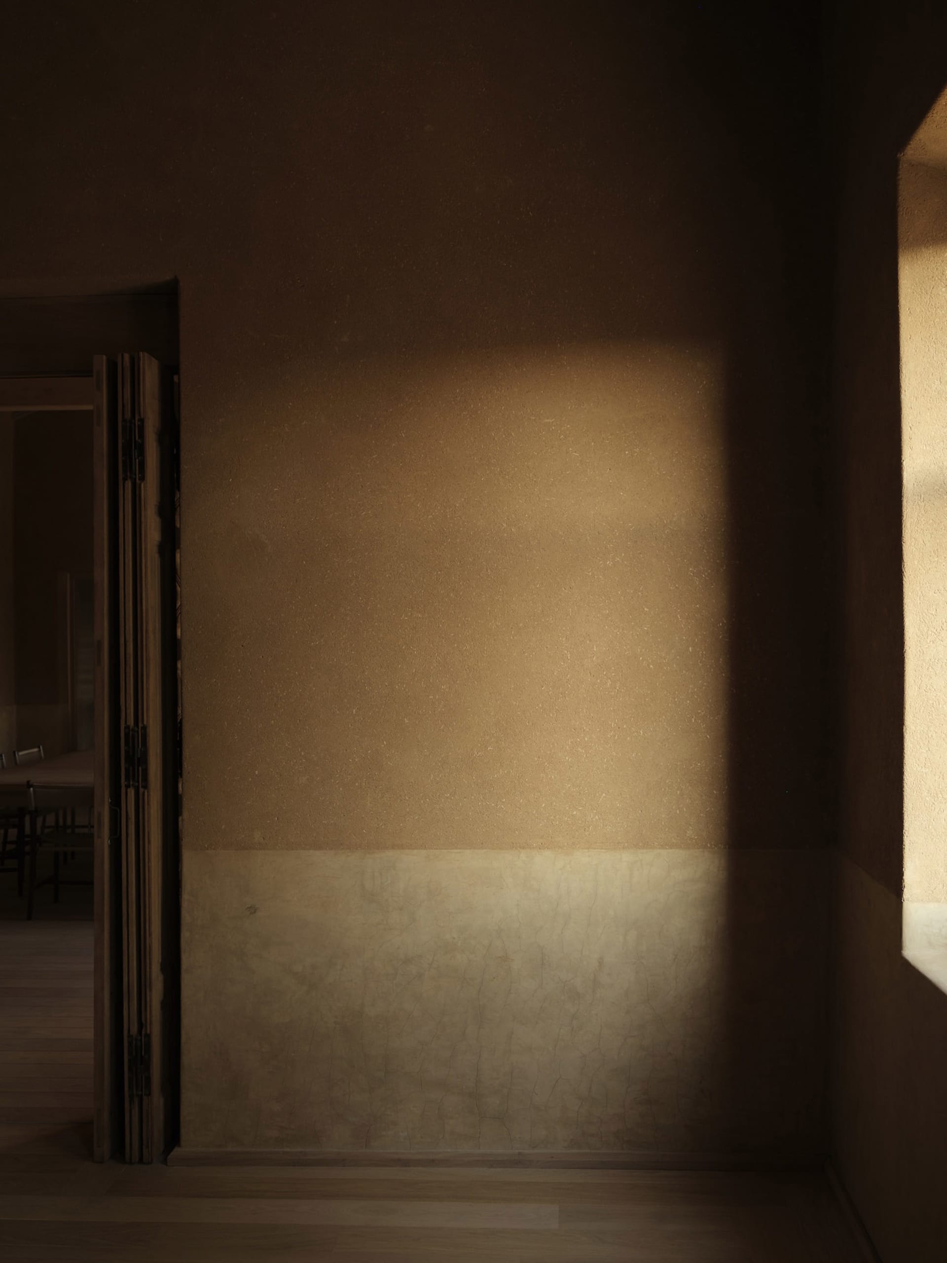 A dimly lit dining area with a stone wall, a dining table, and a chair, with natural light entering through a window