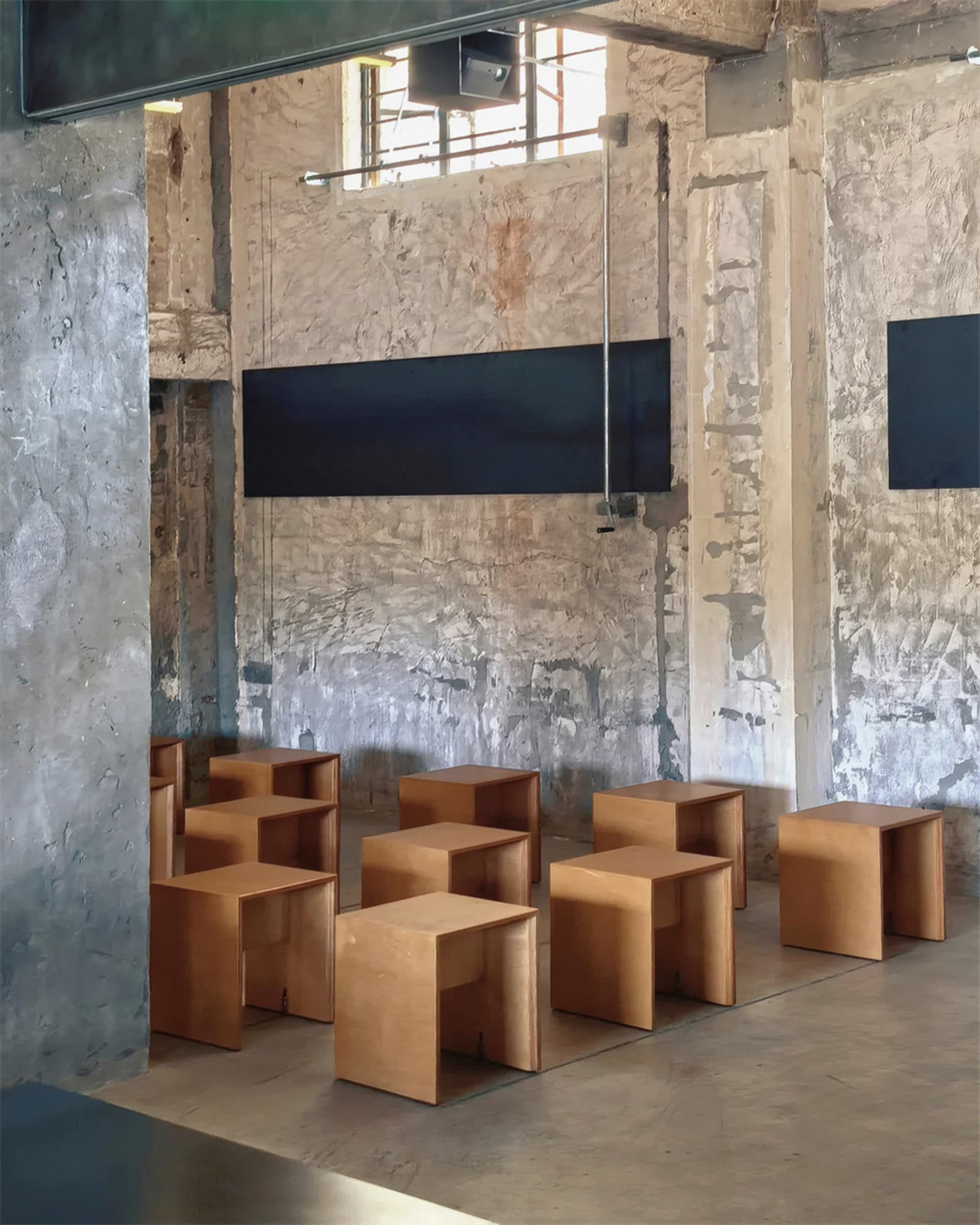 A room with a wooden floor and stone wall features a dynamic arrangement of wooden stools in various sizes and orientations, adding a touch of creativity and playfulness