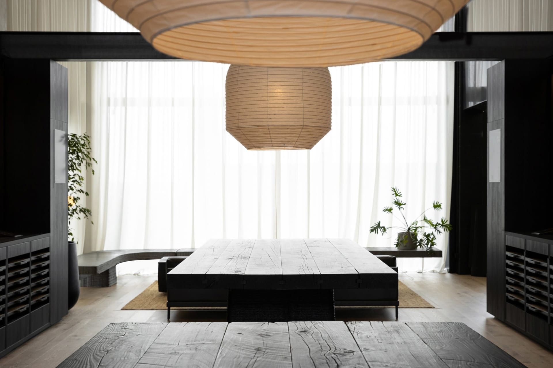 A well-lit living room with a black table and couch, featuring a large hanging light and modern decor